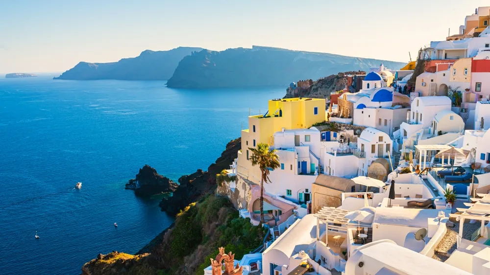 Breathtaking view of Santorini, Greece, with whitewashed cliffside homes, blue-domed churches, and the sparkling Aegean Sea—perfect for a dreamy last minute summer holiday escape.