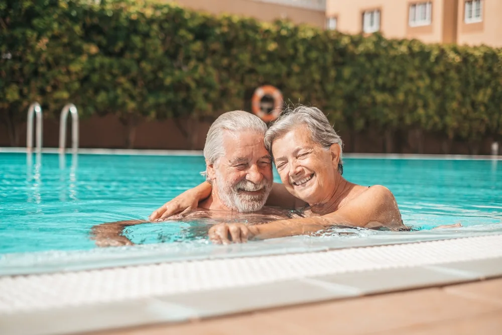Seniors man and women cuddling in a swimming pool abroad - Travel Insurance