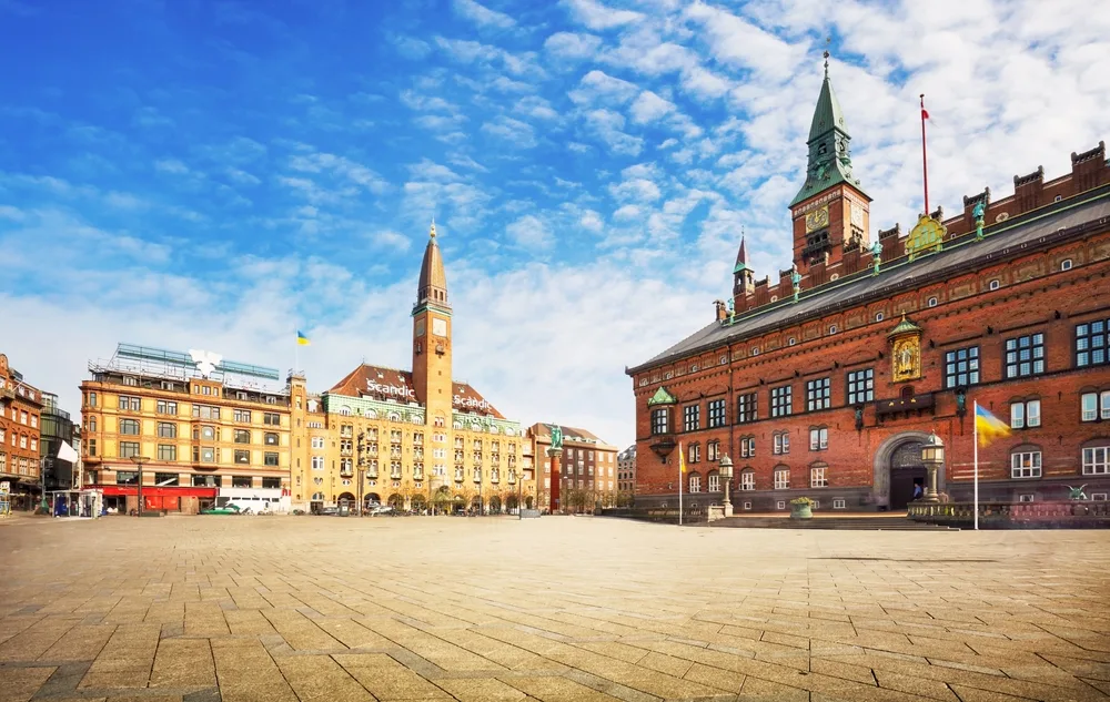 Copenhagen City Hall Square (Rådhuspladsen), Denmark, featuring Copenhagen City Hall’s red-brick facade, clock tower and surrounding historic buildings under a bright blue sky.