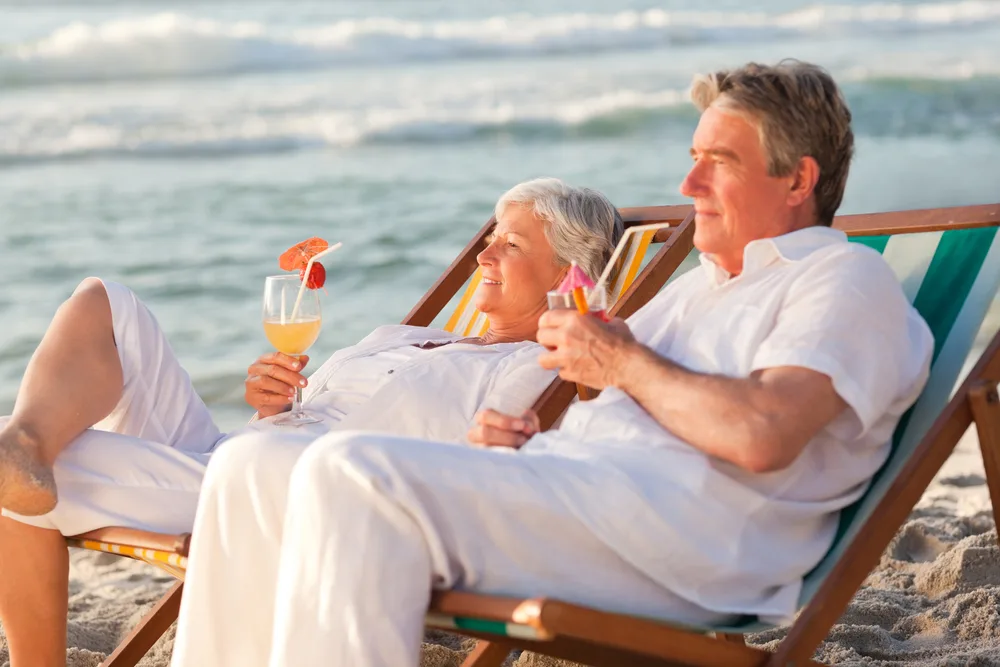 Older couple relaxing on beach chairs by the sea, enjoying drinks at sunset on a summer holiday