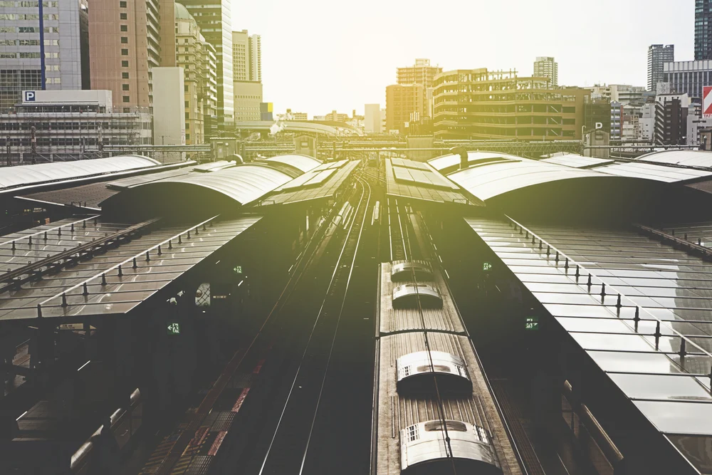 Train platforms at Osaka Station in Japan with modern covered roofs, rail tracks and surrounding city buildings at sunset