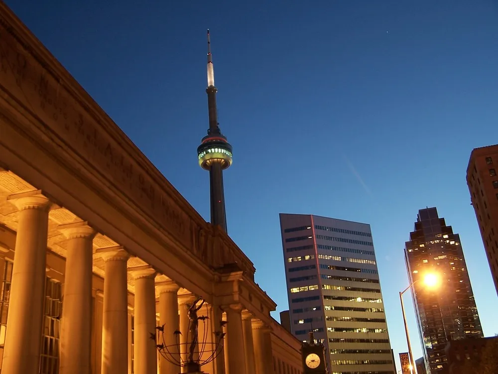 Toronto Union Station with illuminated historic columns and CN Tower rising above the city skyline at dusk