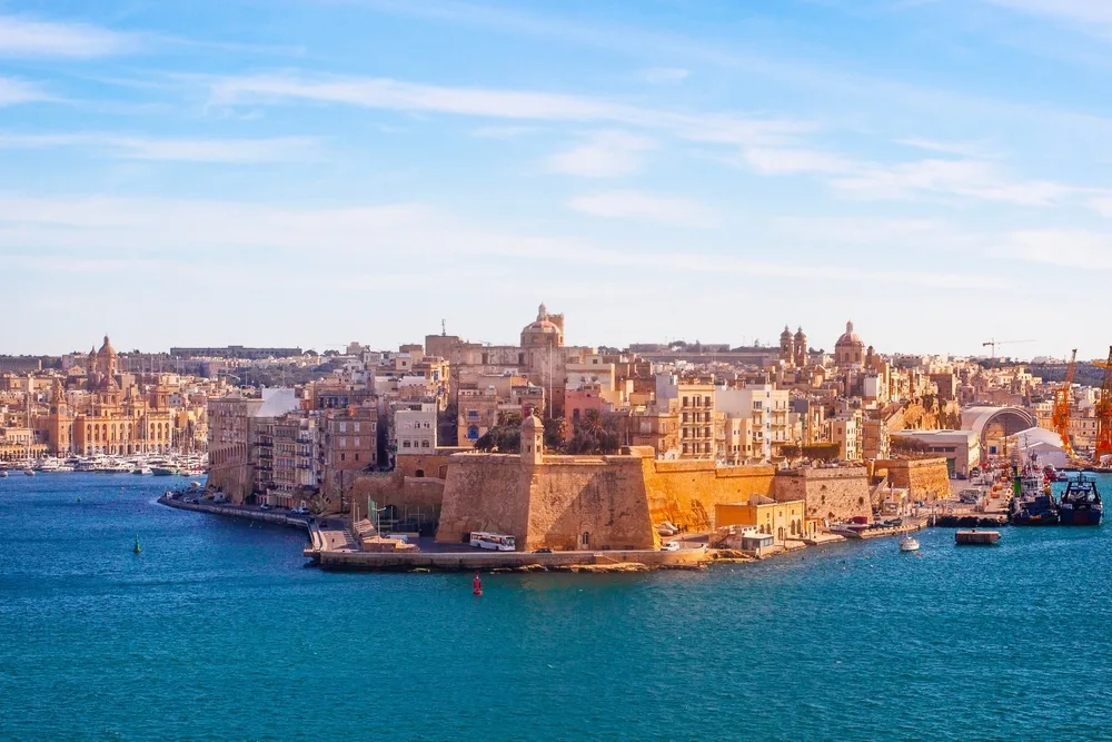 Panoramic view of Valletta, Malta, showcasing historic sandstone fortifications, waterfront buildings, and the Grand Harbour under a clear blue sky.