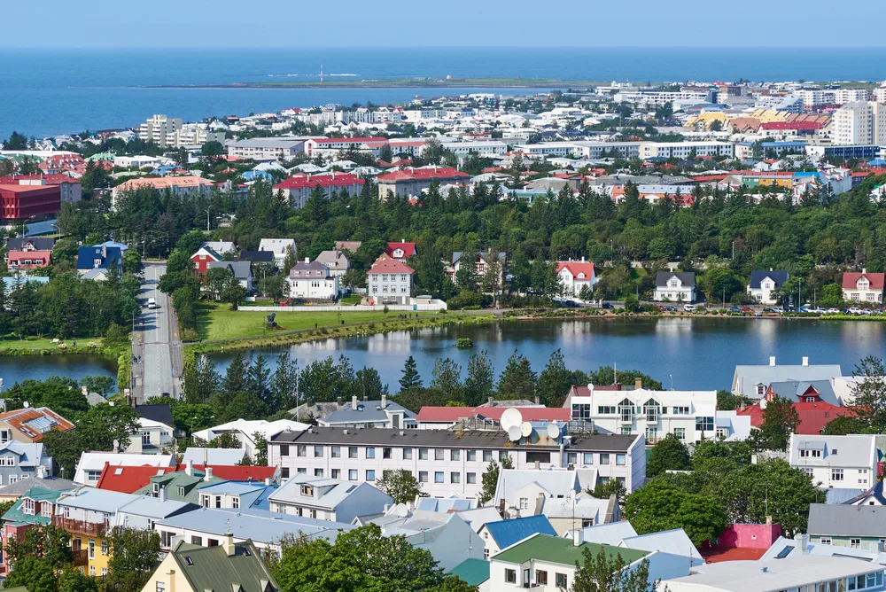 Reykjavik cityscape with colourful rooftops, a peaceful lake, lush green spaces and the Atlantic Ocean in the background on a sunny summer day.
