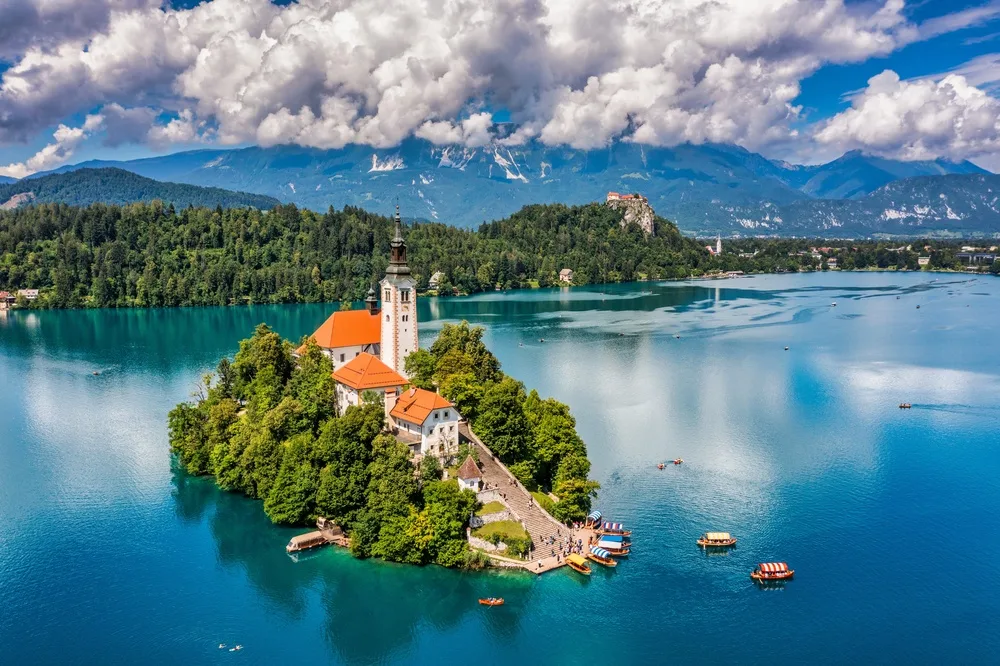 Aerial view of Lake Bled in Slovenia, featuring the iconic church on Bled Island, turquoise water, traditional boats and the Julian Alps in the background.