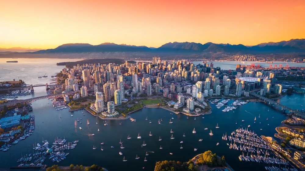 Aerial view of downtown Vancouver, Canada, at sunset, with high-rise buildings, marinas, sailboats and the Coast Mountains in the background.