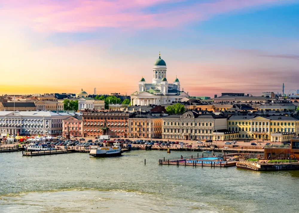 Helsinki waterfront at sunset, featuring Helsinki Cathedral, colourful historic buildings, Market Square and boats along the harbour in Finland.