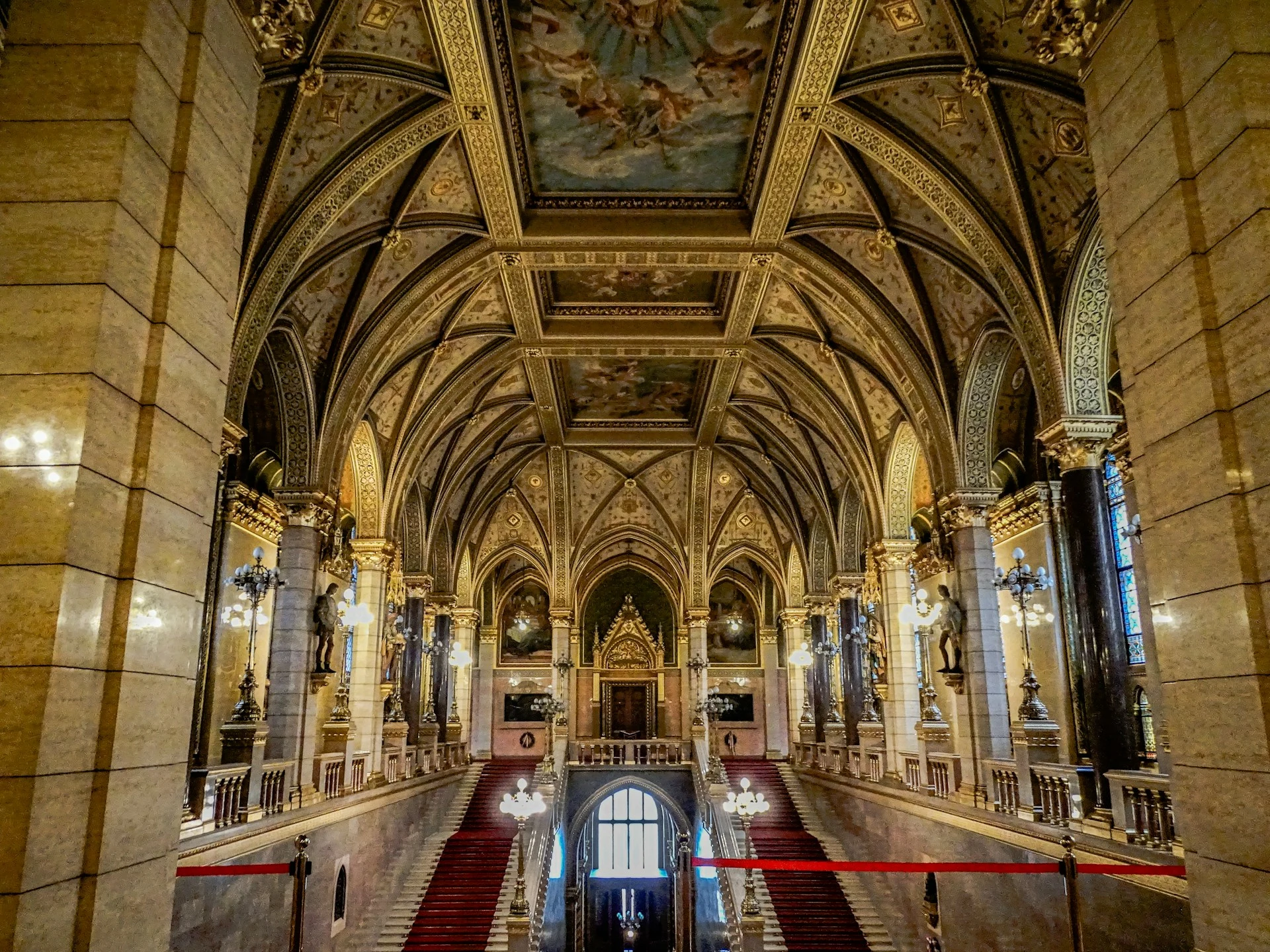 Hungarian Parliament Building interior in Budapest, featuring a grand staircase, ornate vaulted ceilings and gilded architectural details.