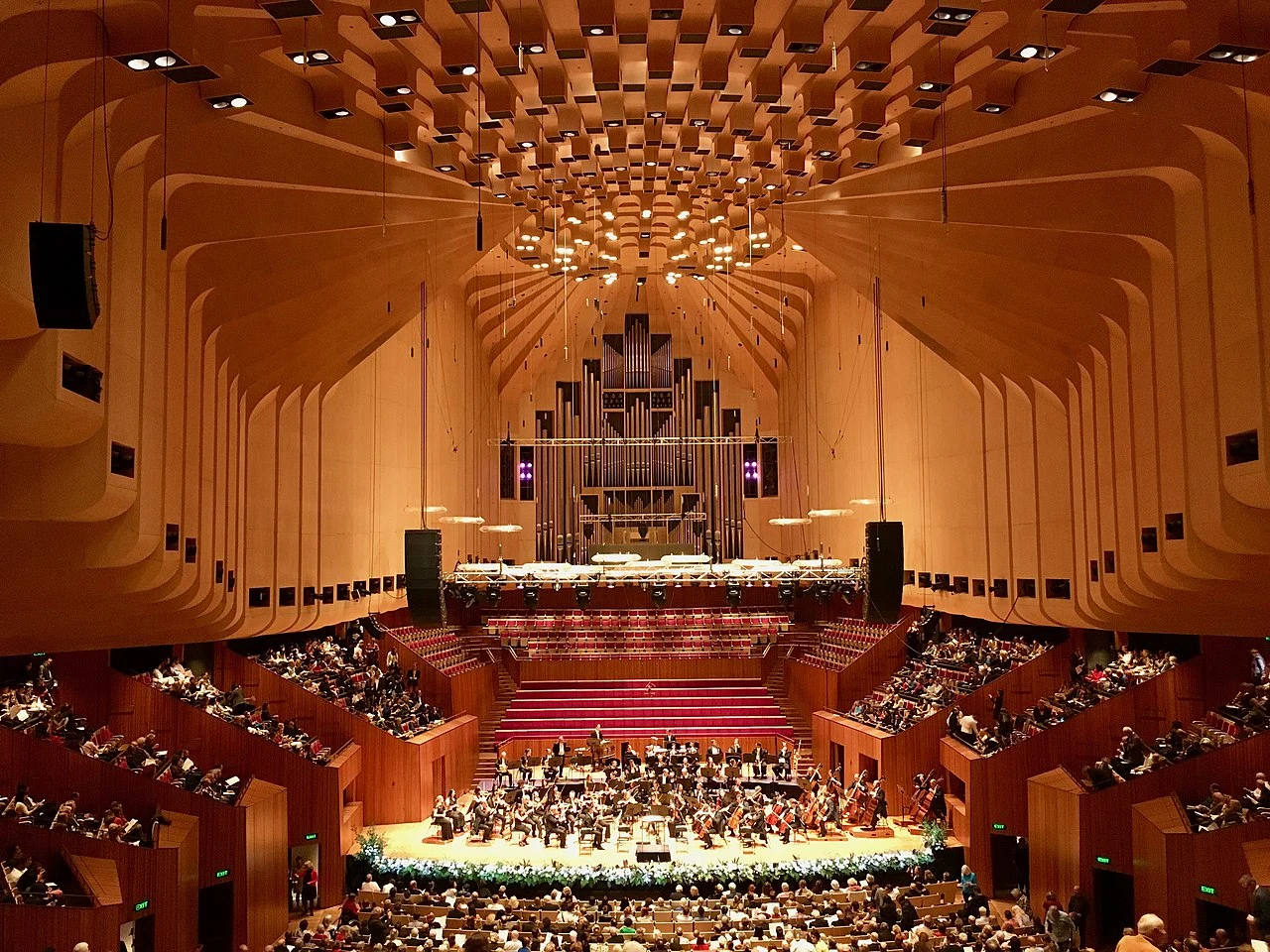 Sydney Opera House Concert Hall interior in Sydney, Australia, featuring its grand organ, timber architecture and orchestra performing on stage.