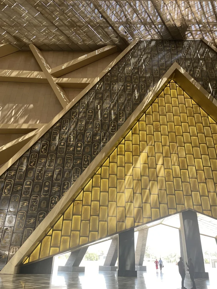 Grand Egyptian Museum interior in Cairo, Egypt, featuring monumental geometric architecture, golden panels and walls decorated with hieroglyphs.