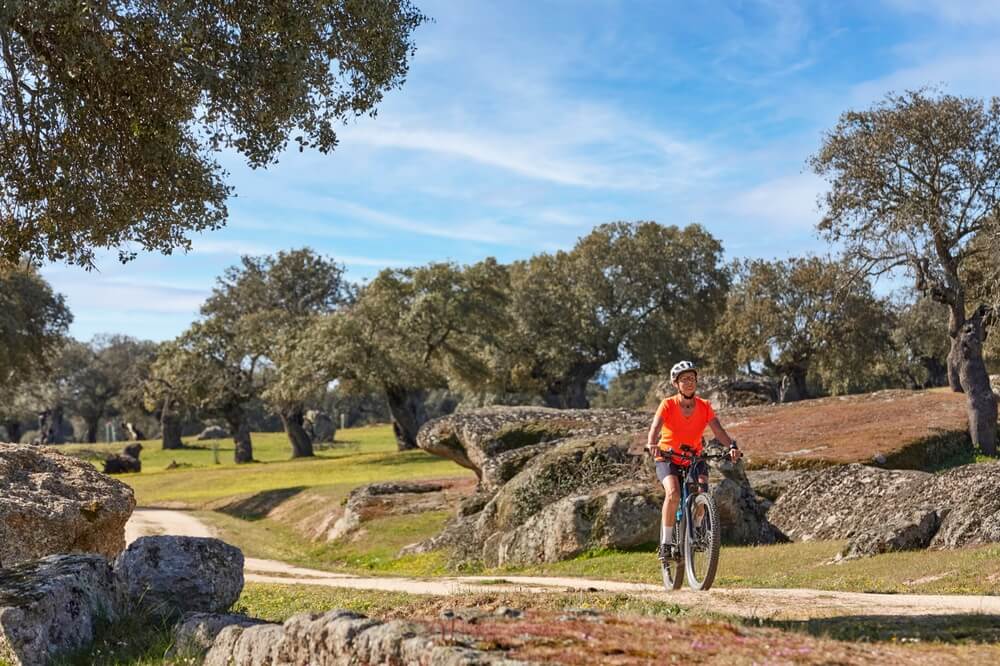 Picture shows a woman cycling past impressive rock formations and trees in the Extremadura region of Spain.