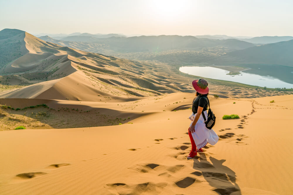 The singing dunes of Badain Jaran in China and Mongolia. A woman looks down on the landscape from atop a dune.