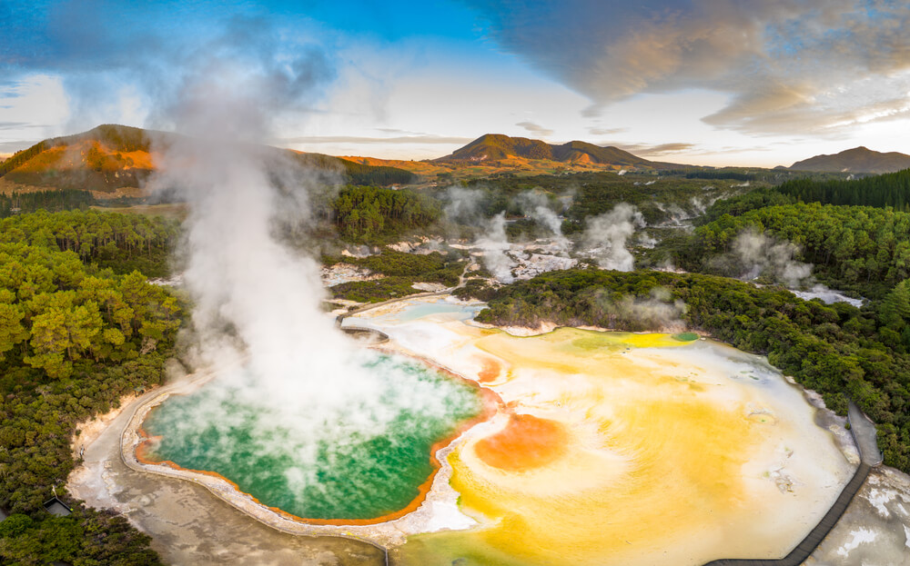 Aerial footage of hot sulphur springs at sunrise, showing colour splashed geothermal reserve of boiling water and steam evaporating in North Island of New Zealand.