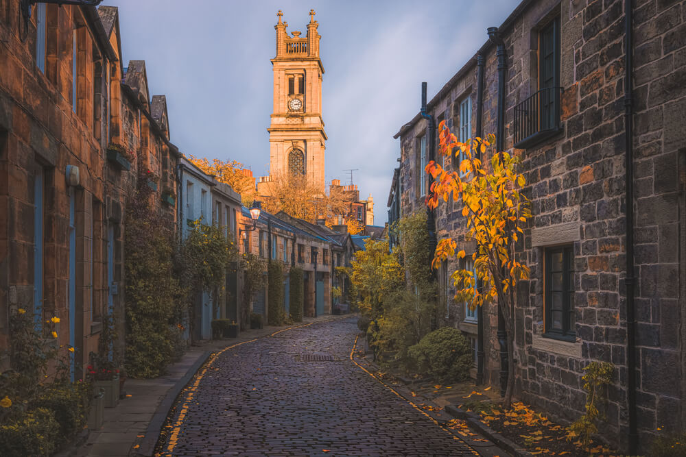 Golden sunset or sunrise light over the picturesque and quaint Circus Lane and St Stephen's Church clock tower with autumn colours in Edinburgh, Scotland