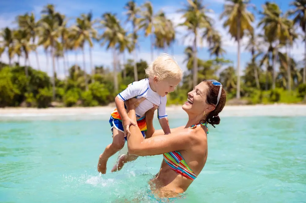 Picture shows a mother and child playing in the clear blue waters off a pristine tropical beach.