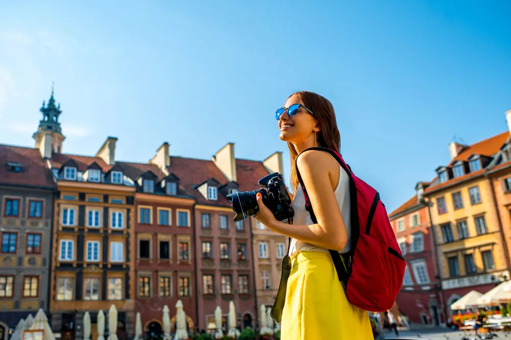 Female traveler with backpack and camera in the old town market square in Warsaw, Poland.