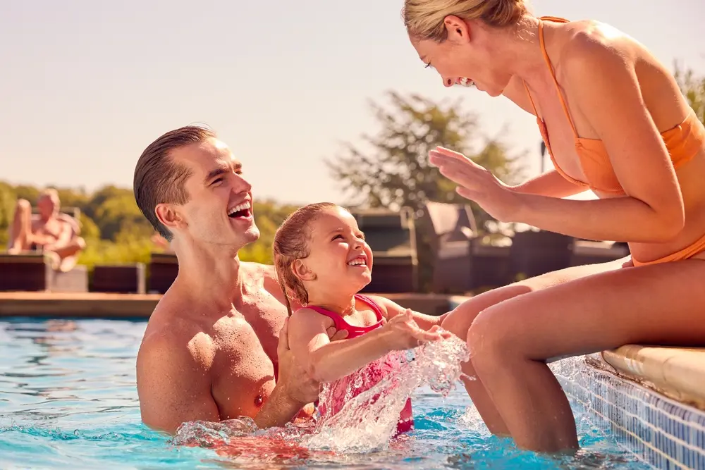 Smiling Family On Summer Holiday Playing In Swimming Pool.