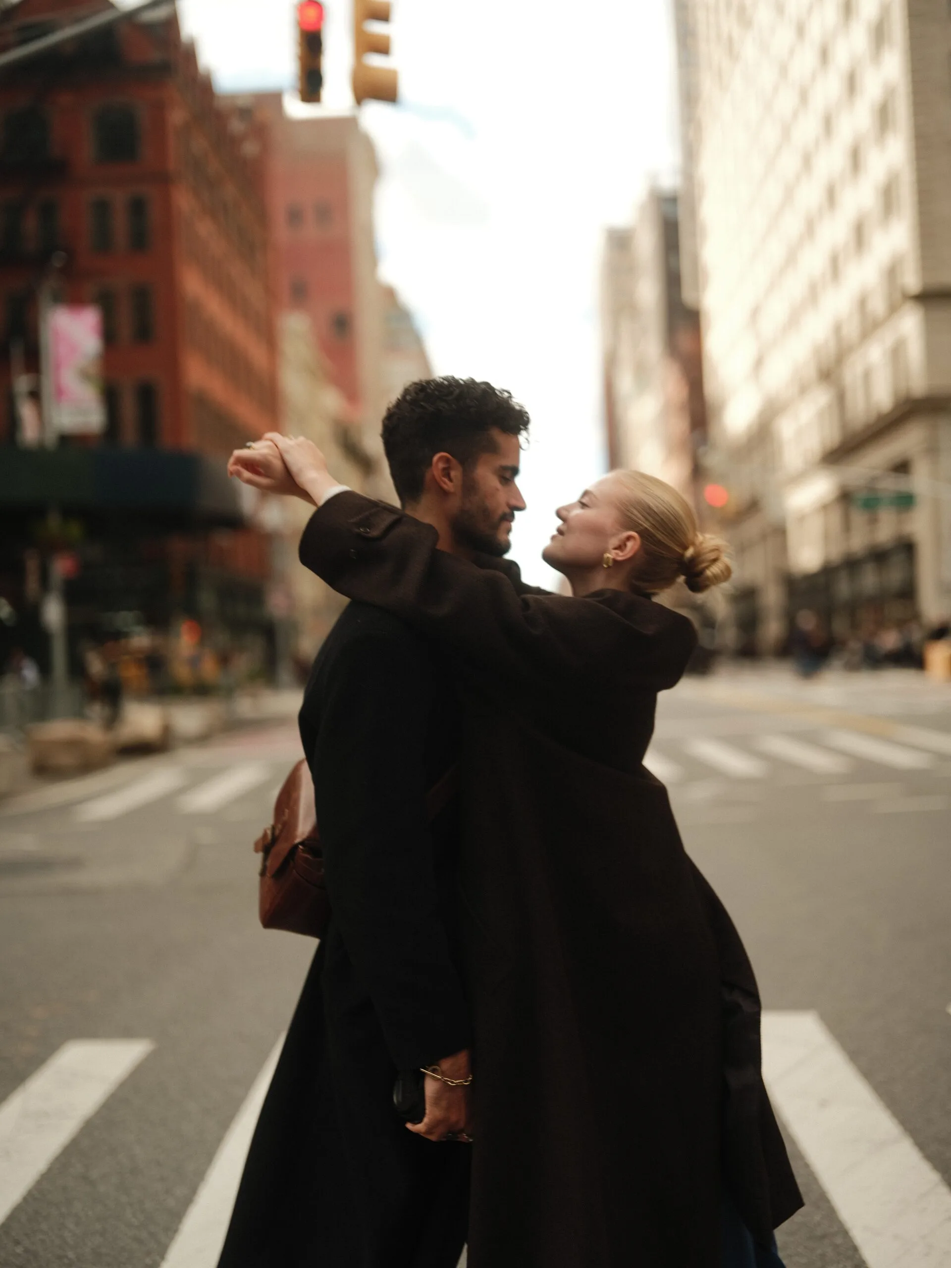 A couple lifted in a kiss mid-crosswalk on Fifth Avenue, pedestrians and a taxi blurring past in black and white.