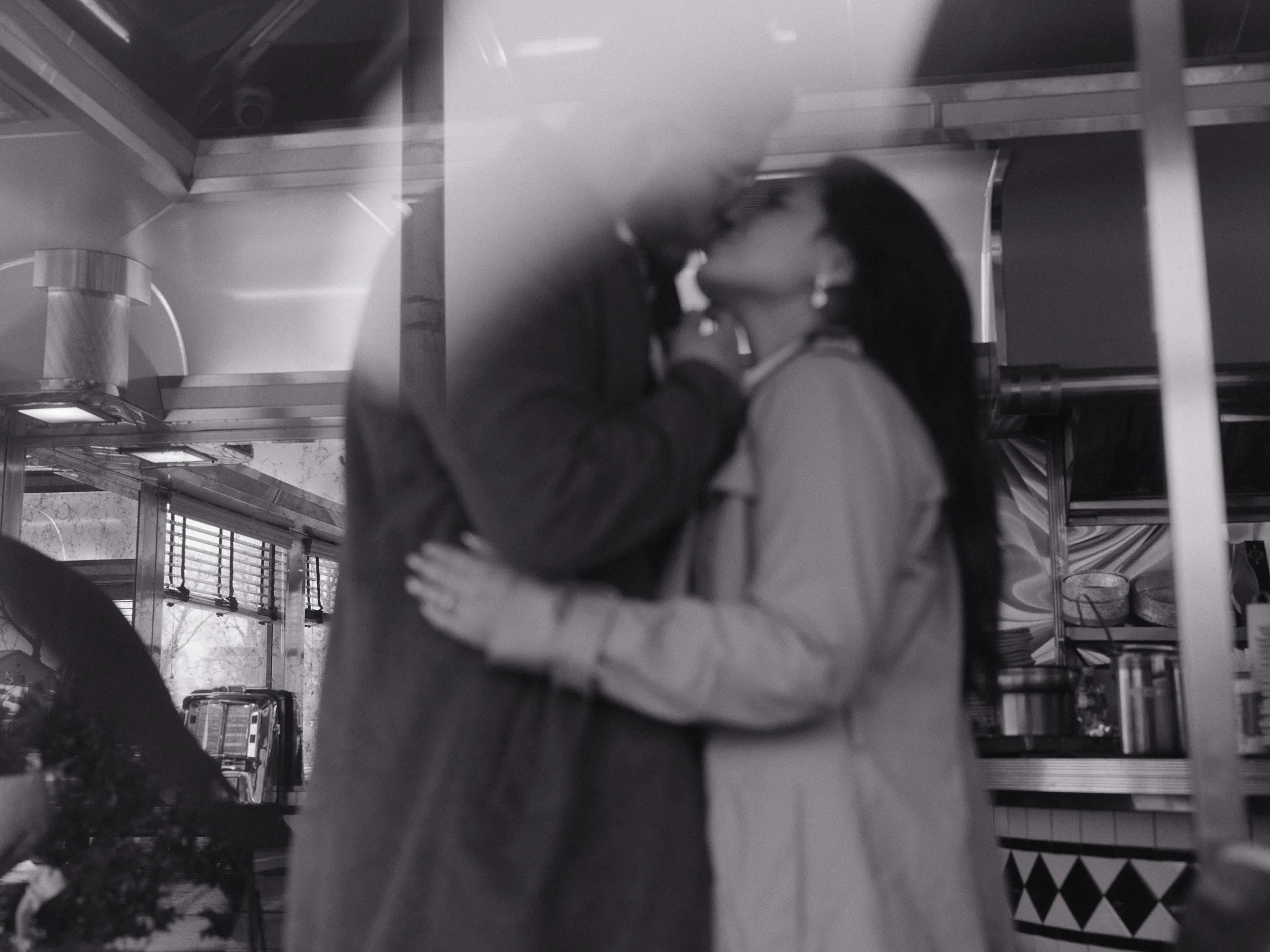 At the diner counter — a kiss through a film of motion blur, kitchen behind.