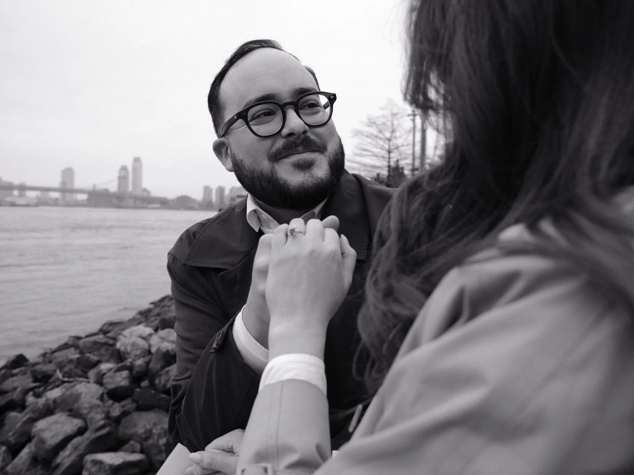 A couple on the Brooklyn waterfront, Manhattan skyline in fog behind them.