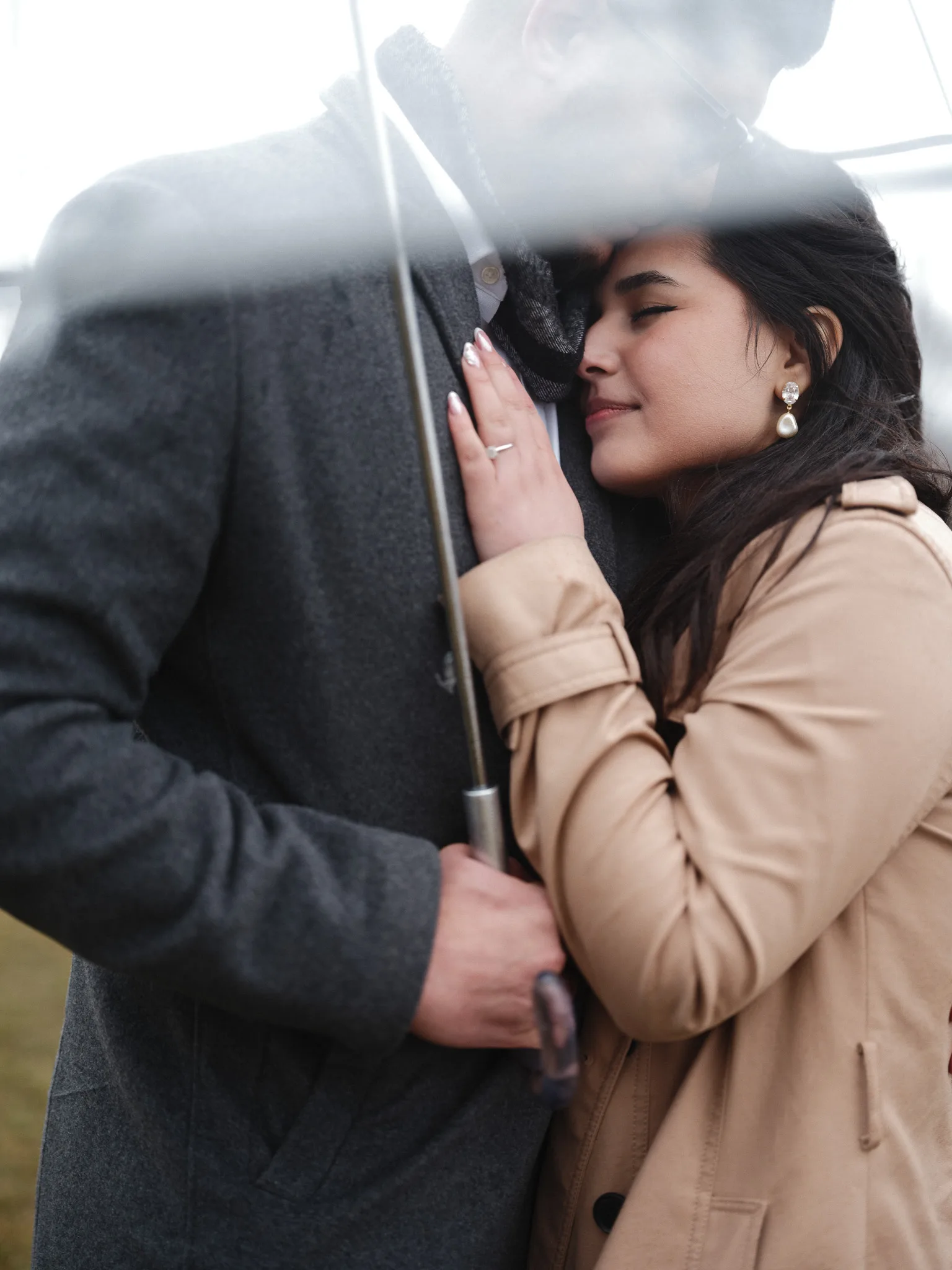 Tender hug under the umbrella — her ring hand on his lapel.