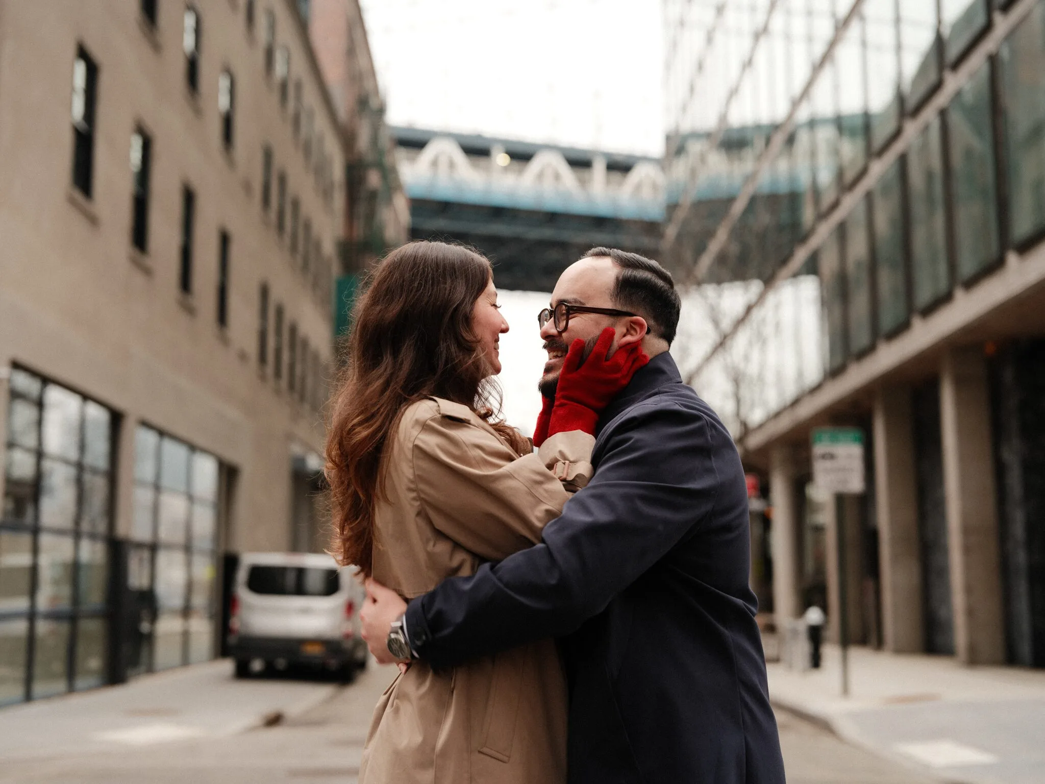 Embracing between two Dumbo buildings — Alfredo's face caught by a red glove, the blue Manhattan Bridge crossing high between the facades.