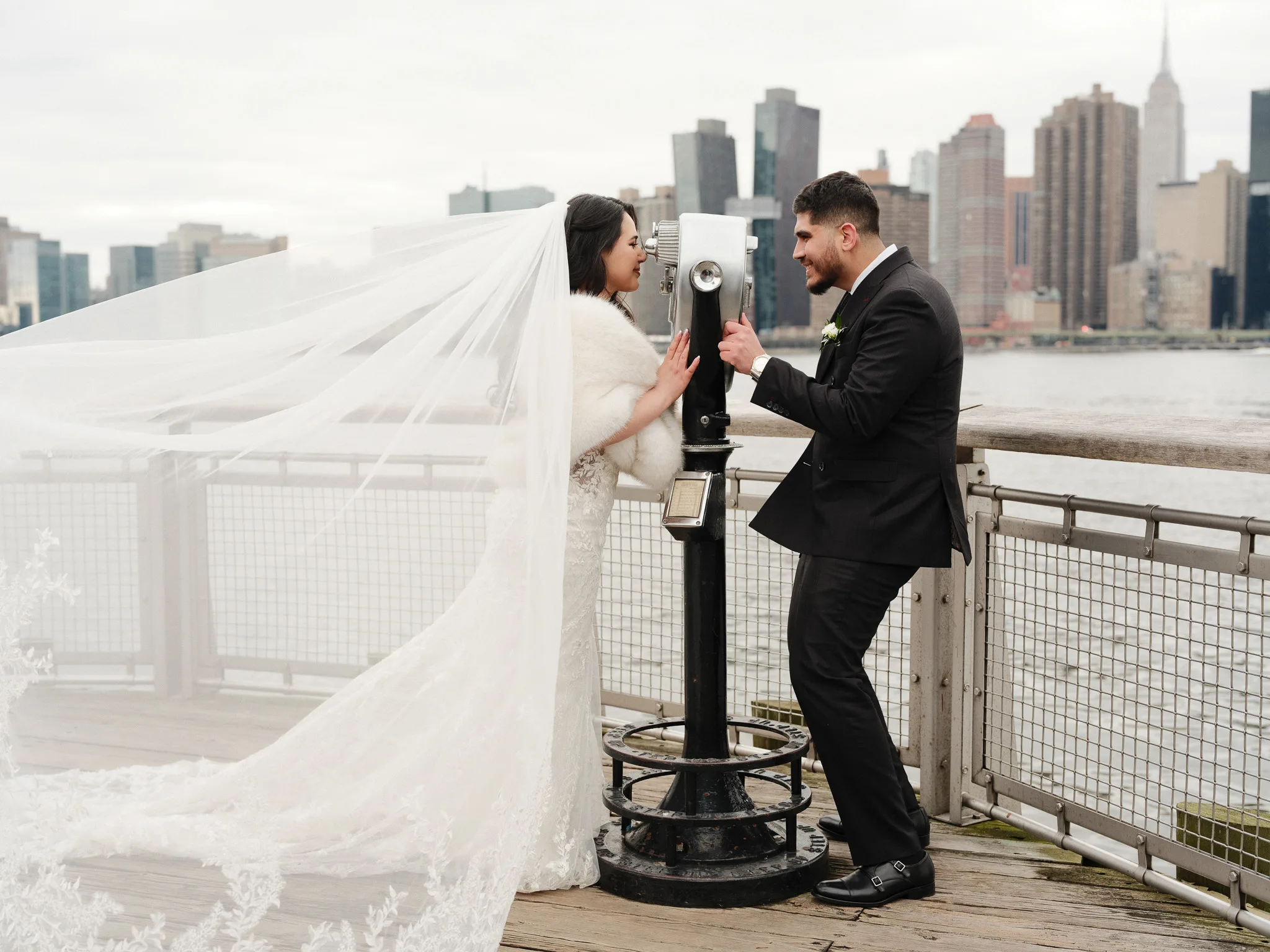 Close kiss — her veil falling in the foreground, the river soft behind them.