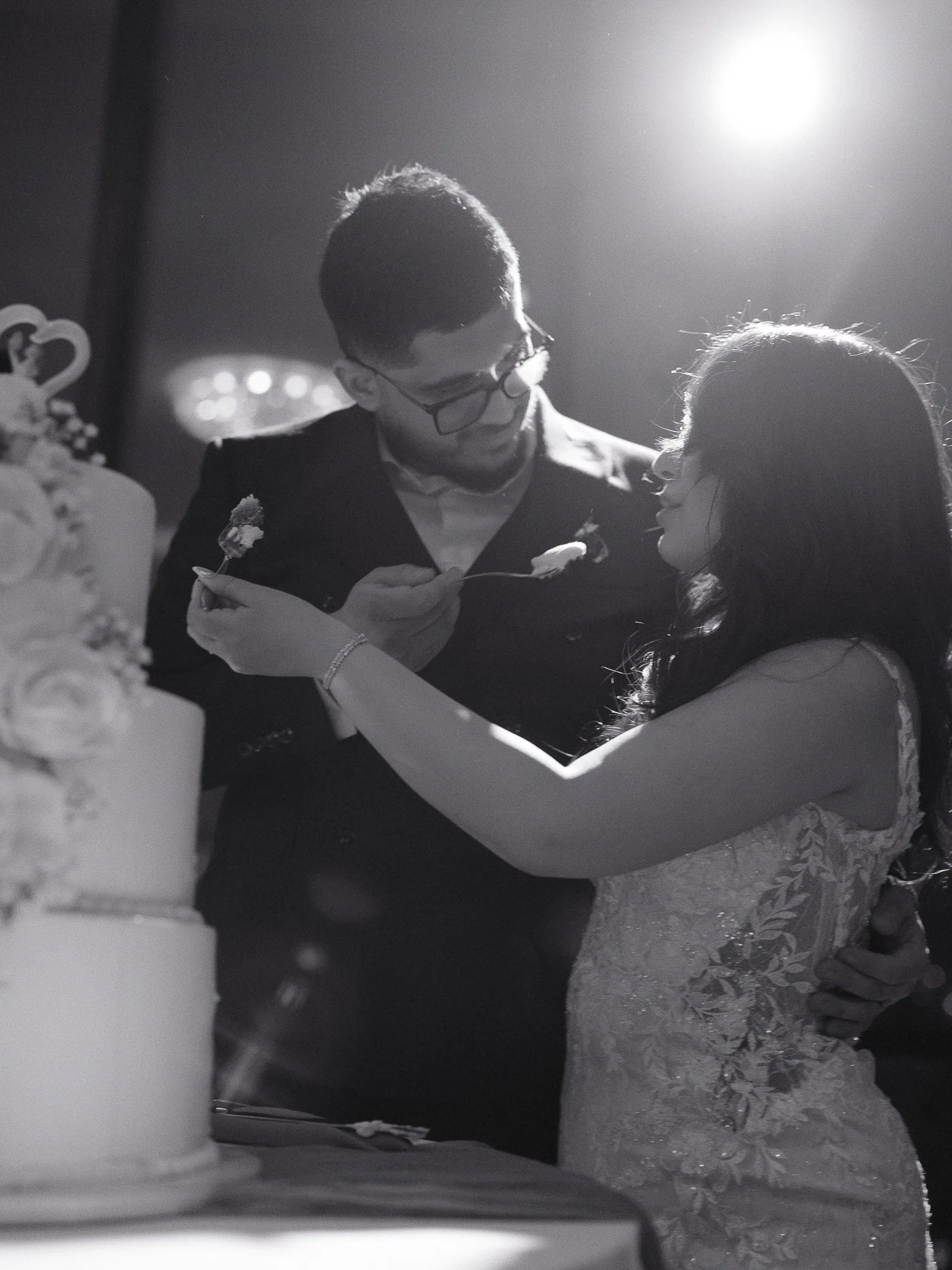 Cake-cutting — a forkful of frosting, both of them laughing, the light of the room blown out behind.