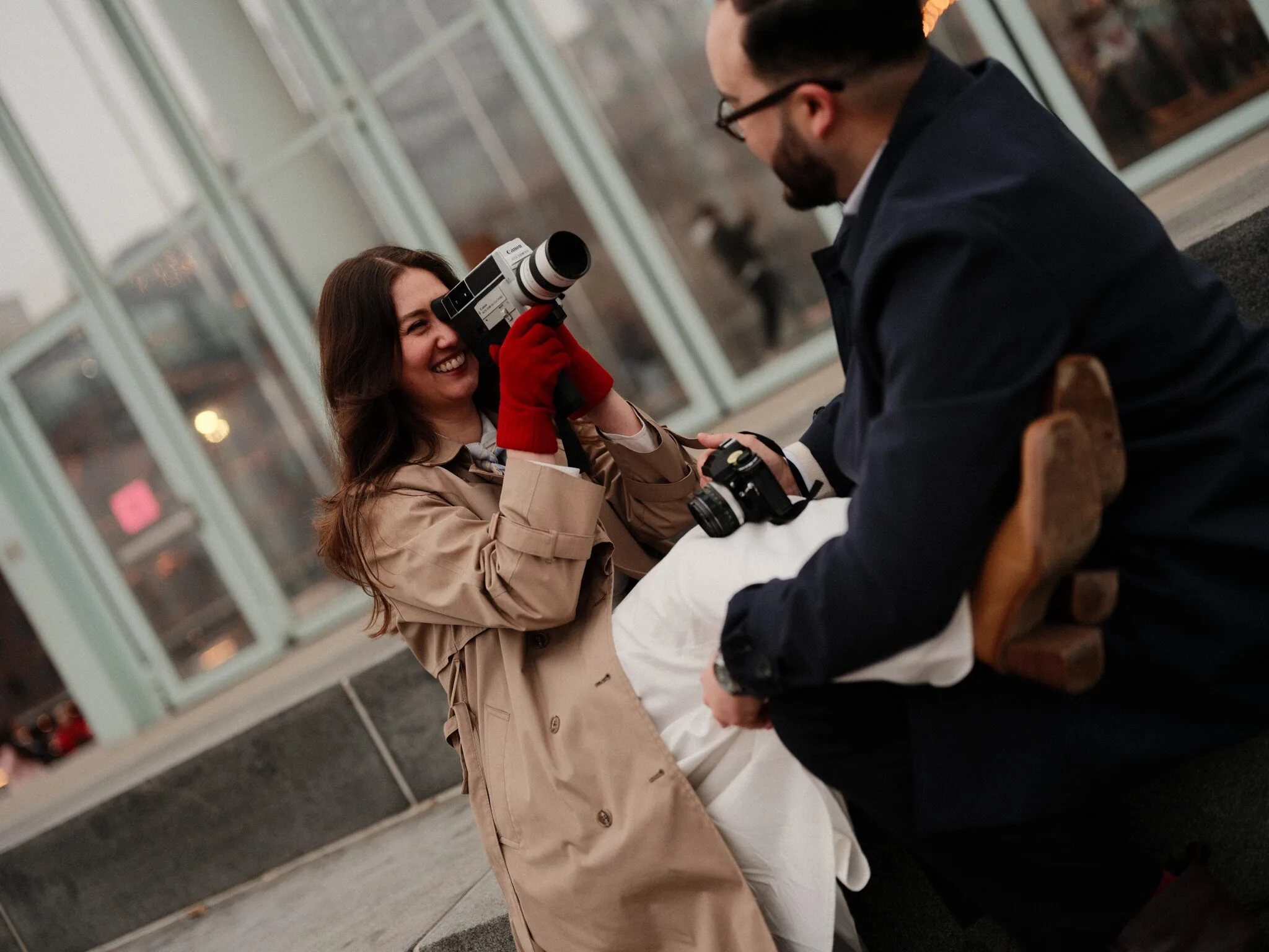 Couple laughing together while holding a vintage film camera on a city sidewalk