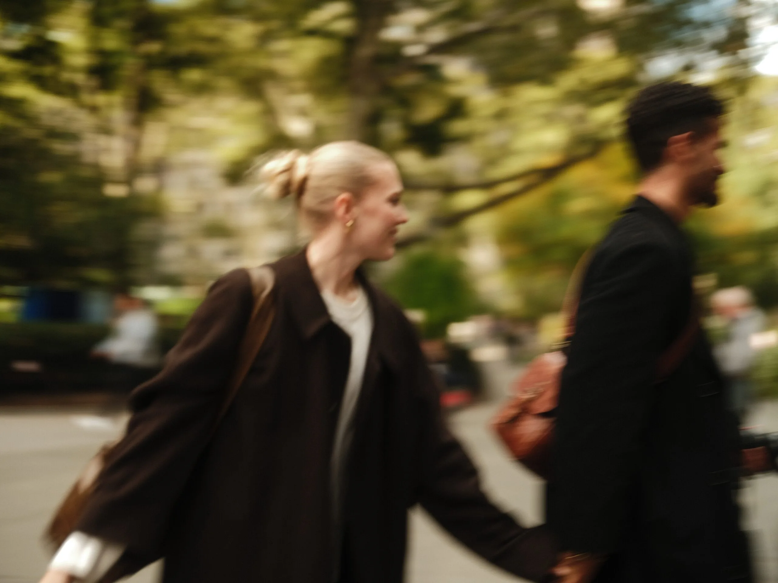 The couple reach across each other crossing a Manhattan street, coats wide.