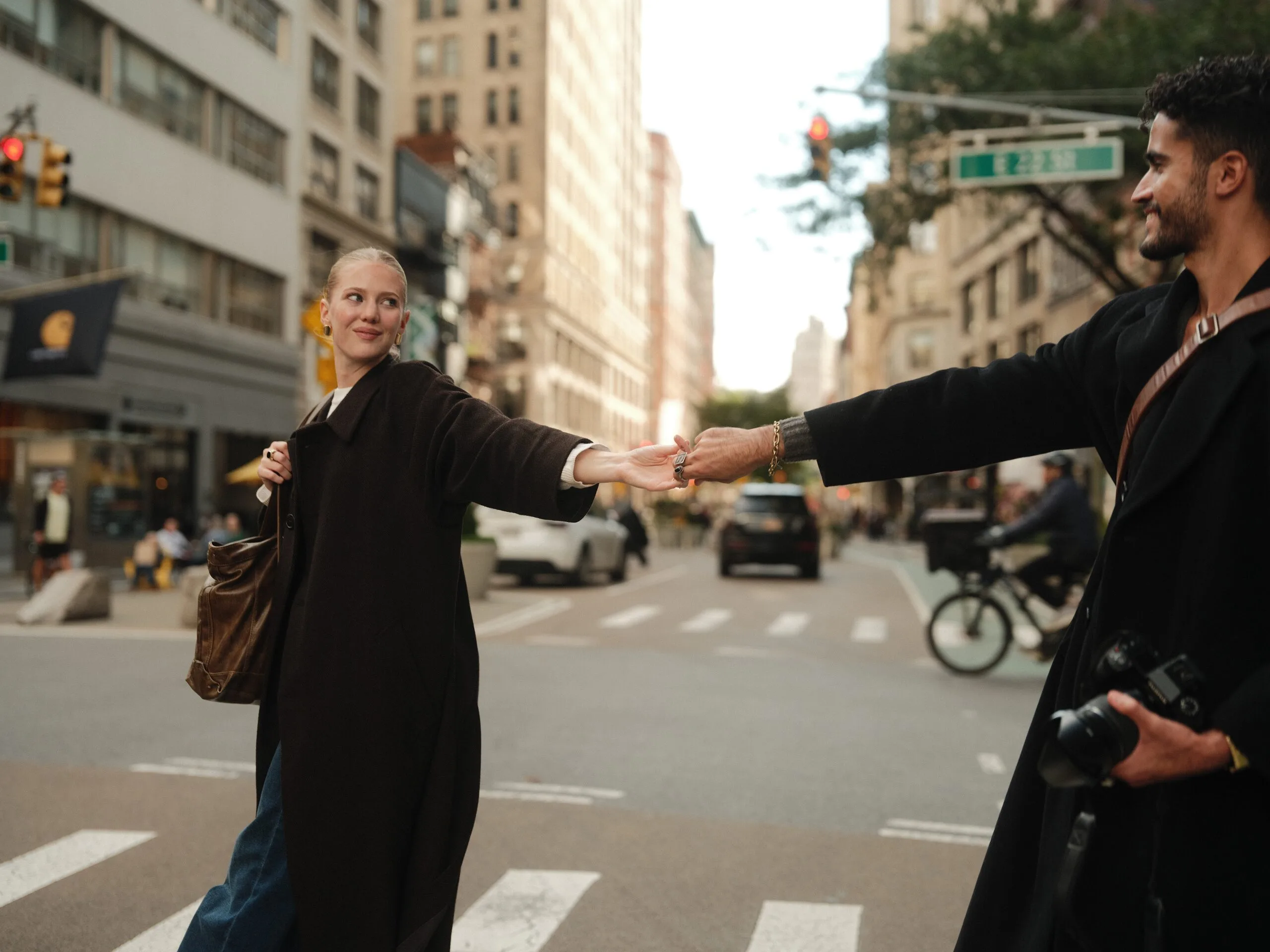 Wide street scene — the couple meet mid-crosswalk with the Flatiron beyond.
