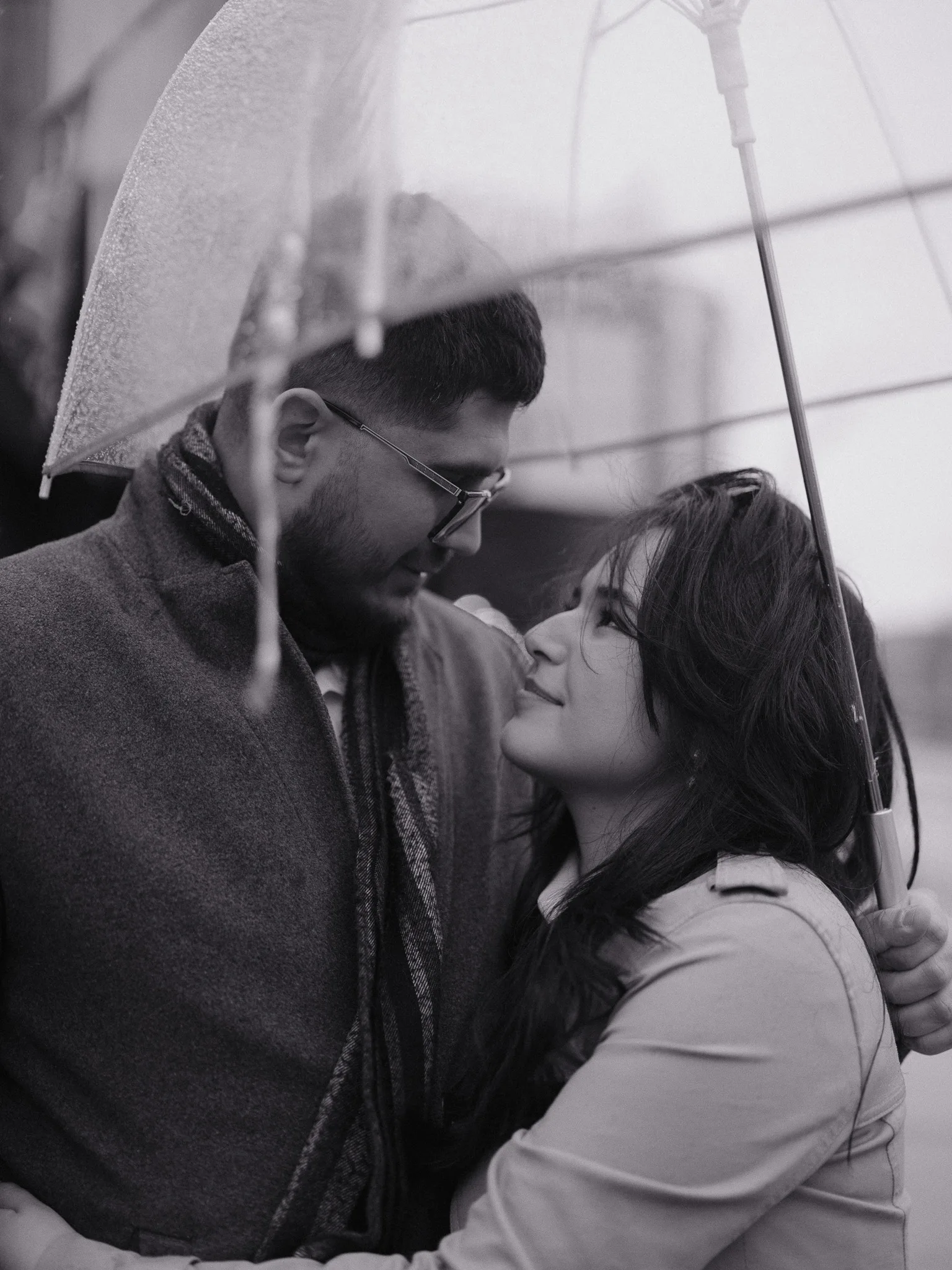 Under a clear umbrella, foreheads close — Bayron and Scarlett look at each other in the rain.