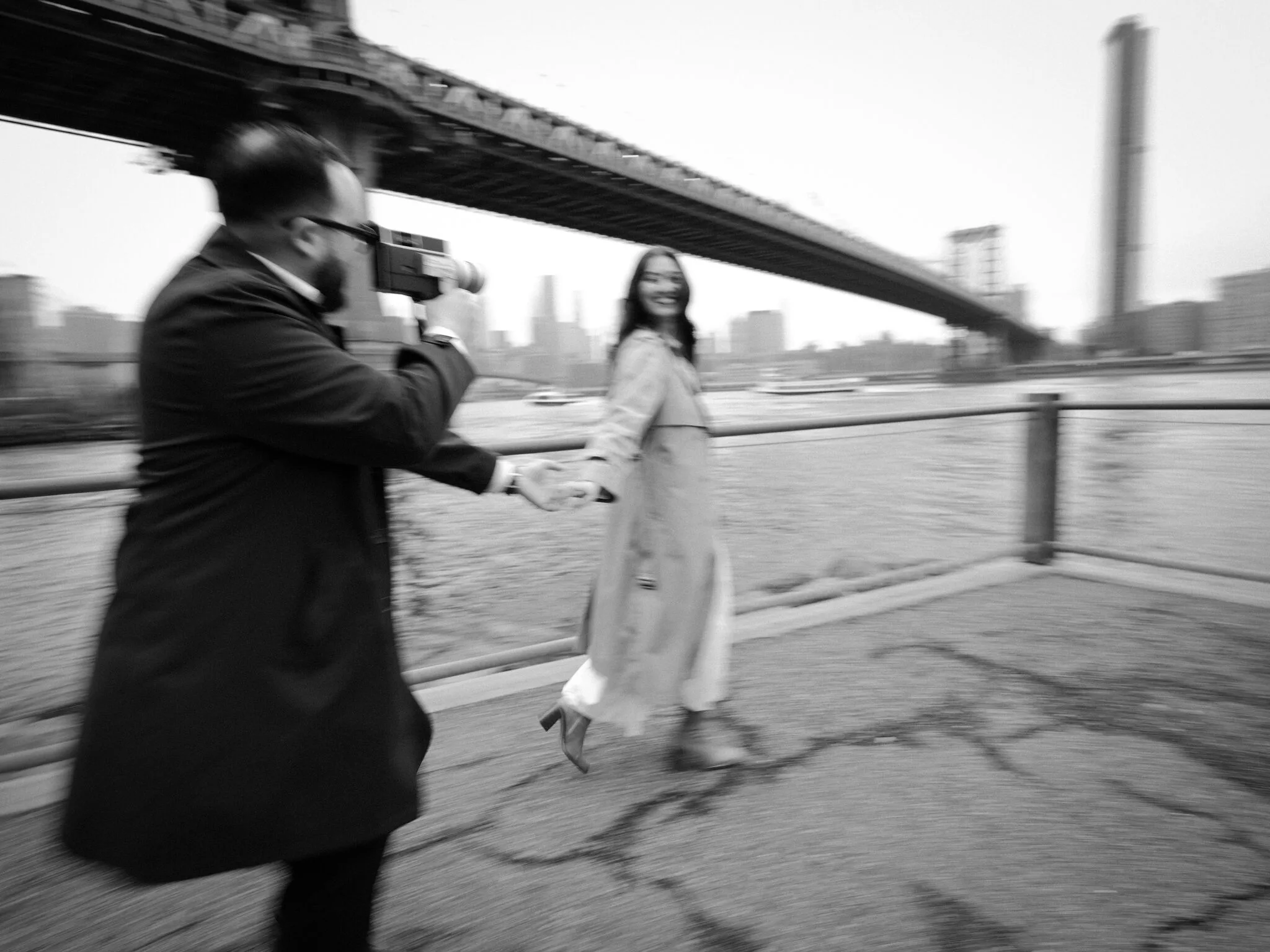 Motion blur in black-and-white — Alfredo photographs Lexi as she walks past him, both moving, the Manhattan Bridge blurring overhead.