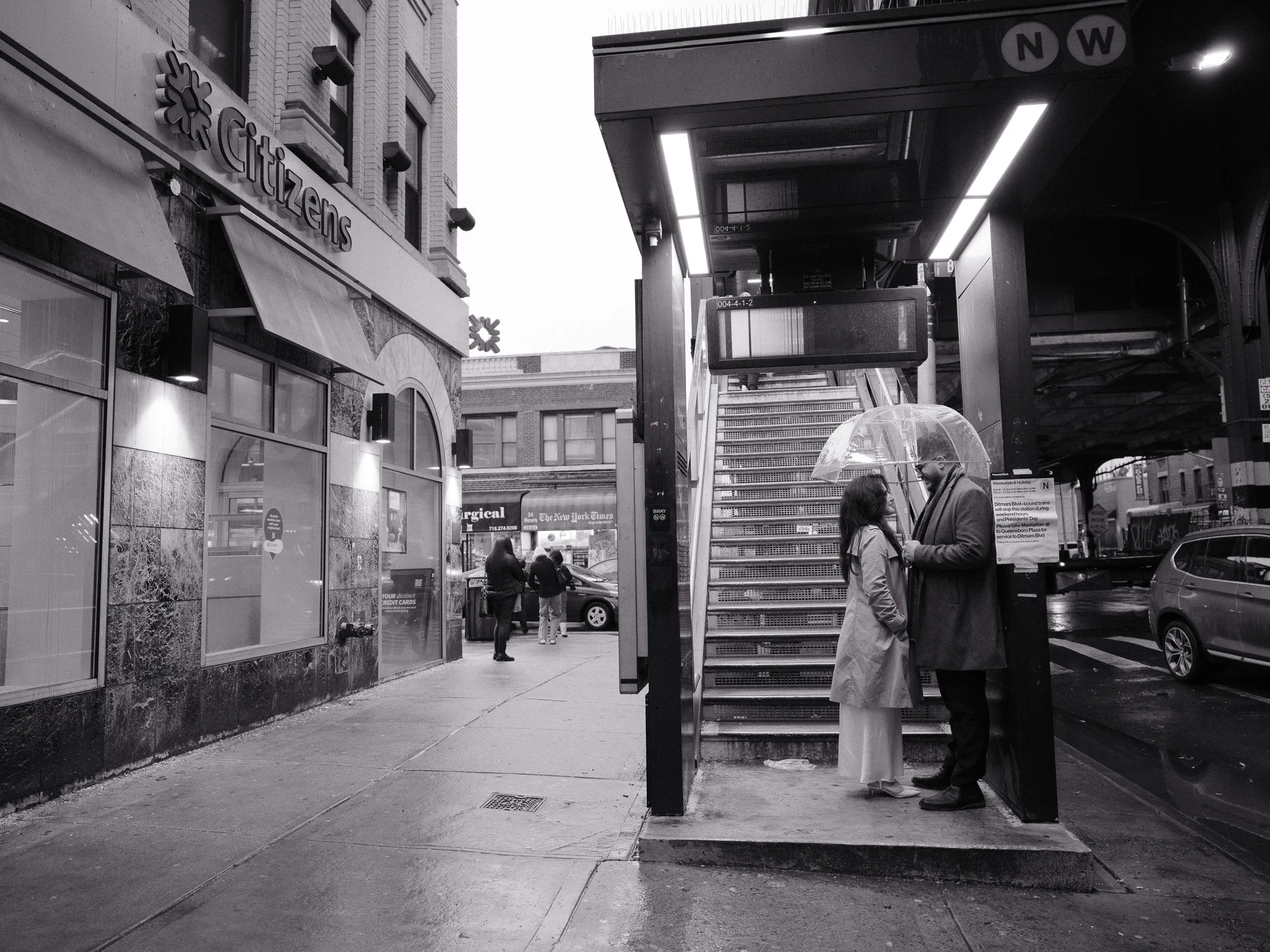 Scarlett and Bayron talking at the foot of an N/W subway stair, Citizens bank across the street.