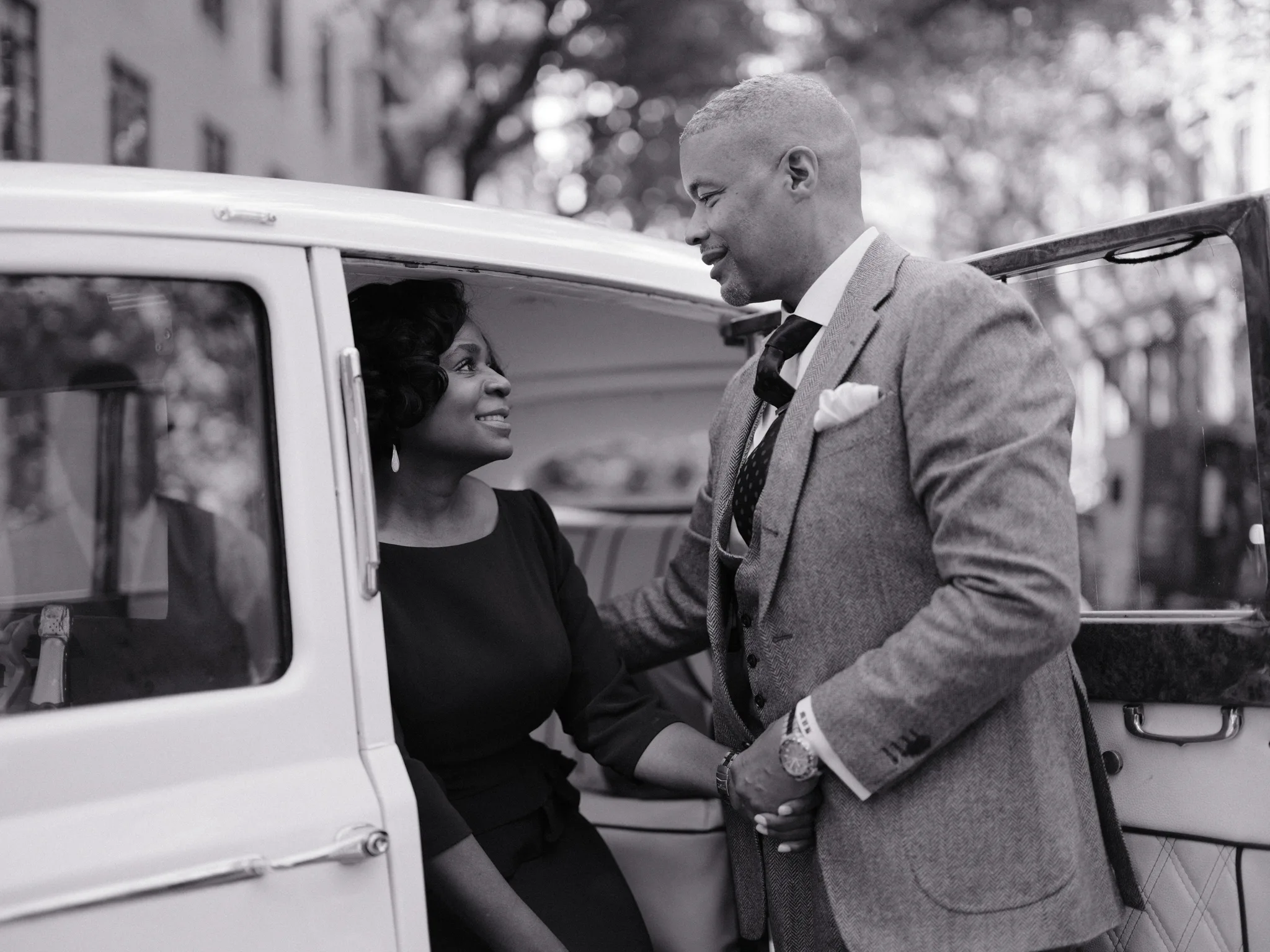 Couple sharing a moment beside a vintage car, black and white editorial portrait