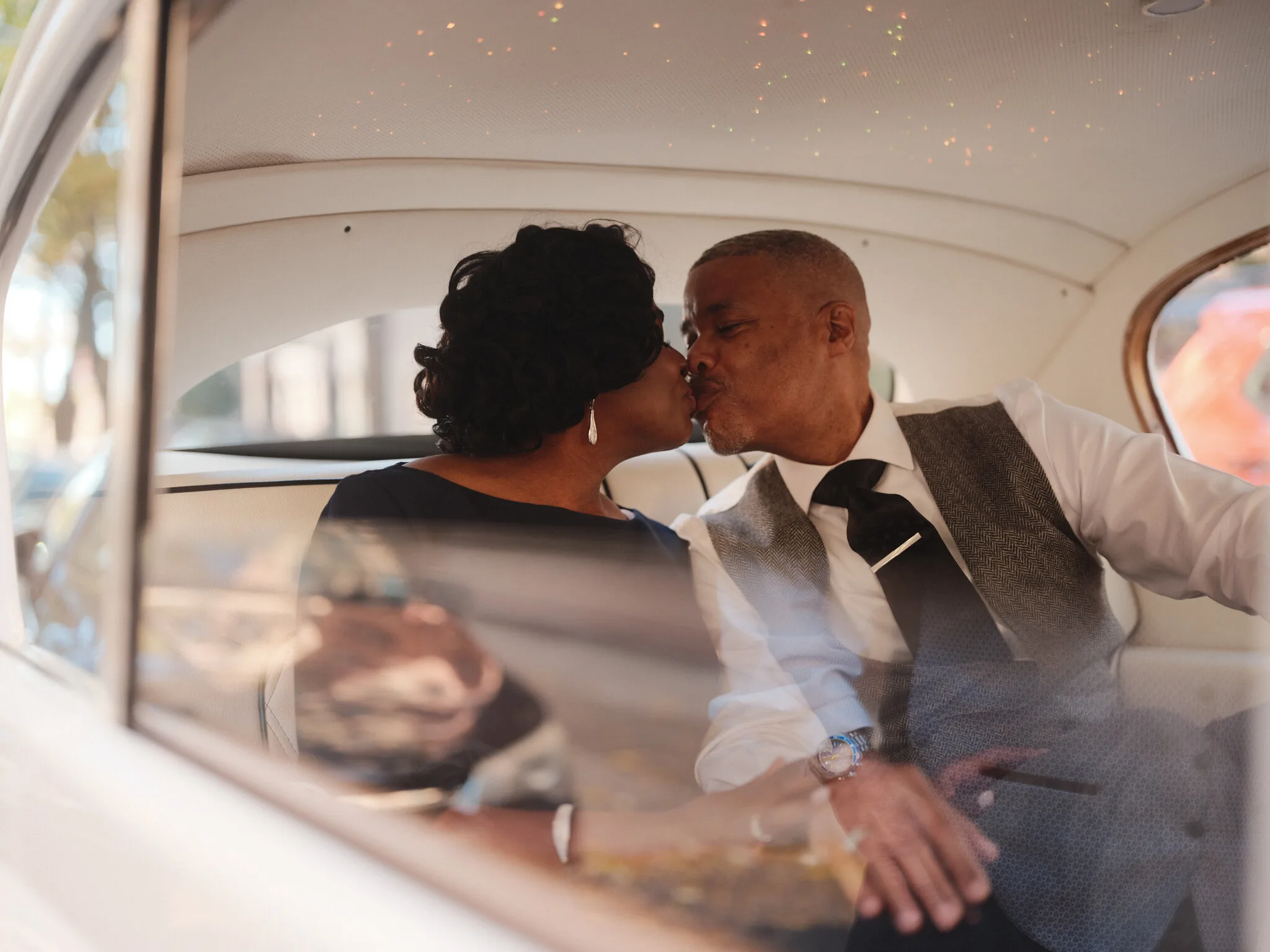 Marc and Olgeta kissing inside the Rolls, cream interior, intimate.
