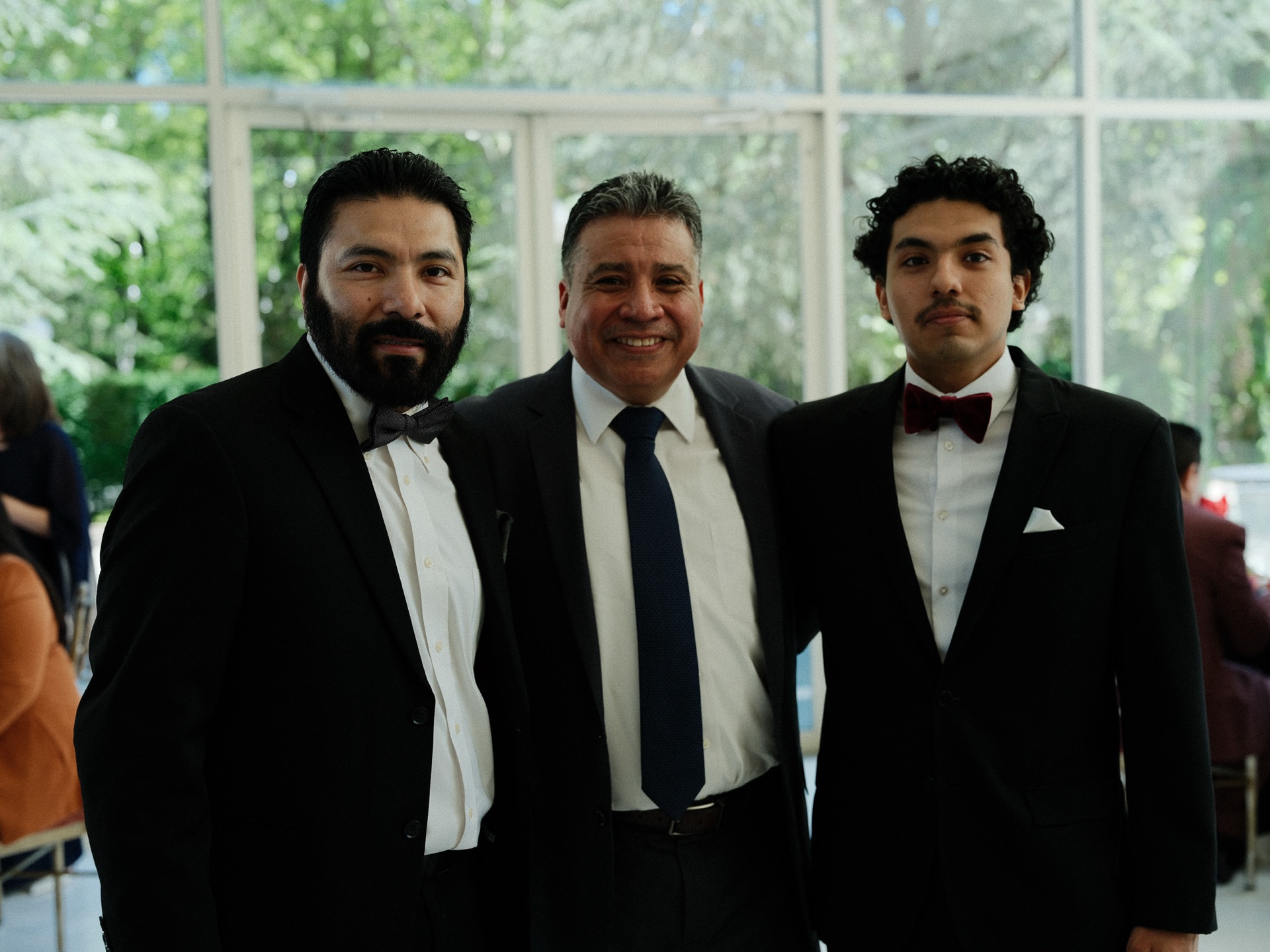 Three of the men in the family side-by-side in formal black-tie, between the columns of the conservatory.