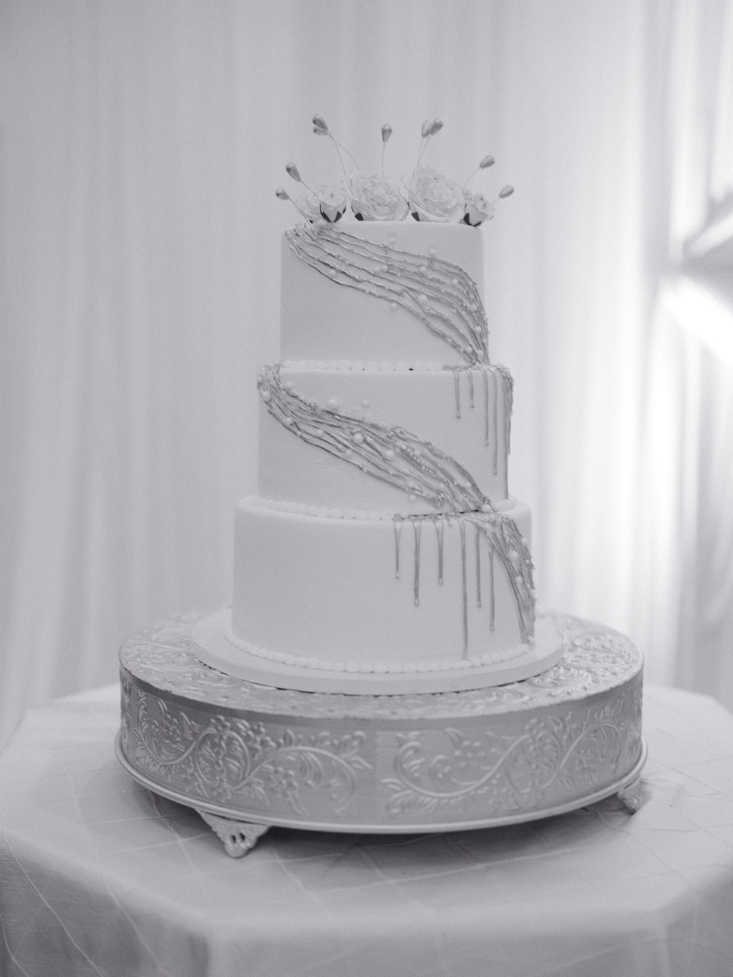 Three-tier white anniversary cake on a silver stand with gold-tipped sugar flowers
