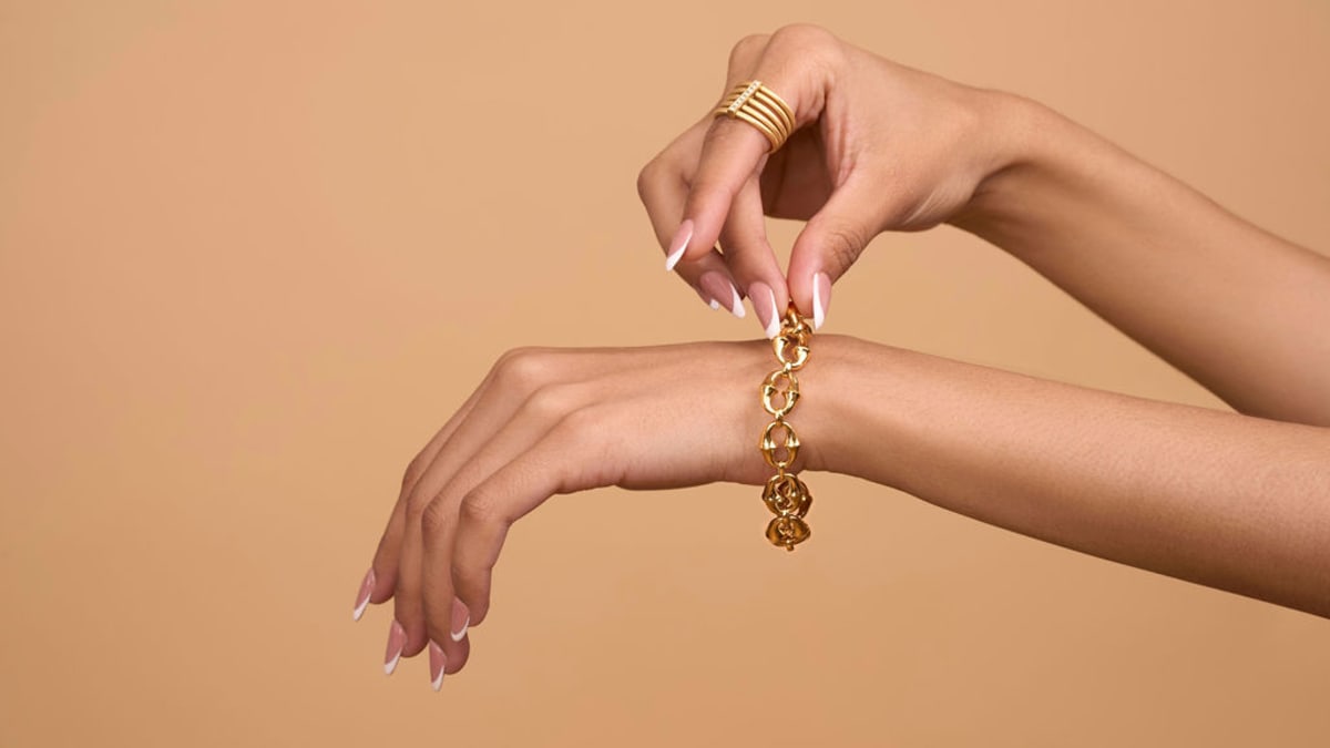 Gold bracelet and ring styling detail against a warm backdrop