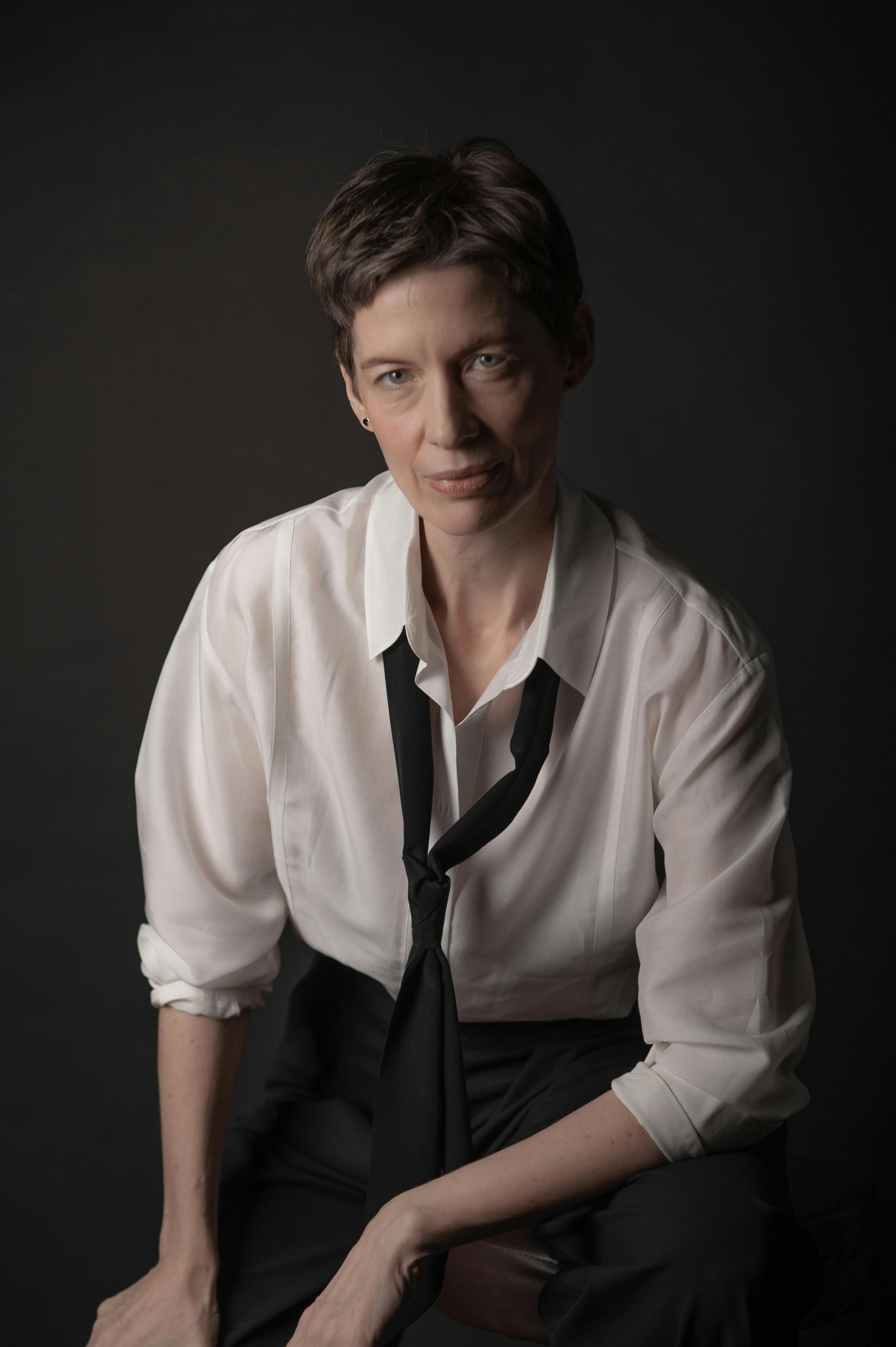 Professional portrait of woman with short hair in white shirt and black tie on dark background demonstrating creative professional portrait style for personal branding