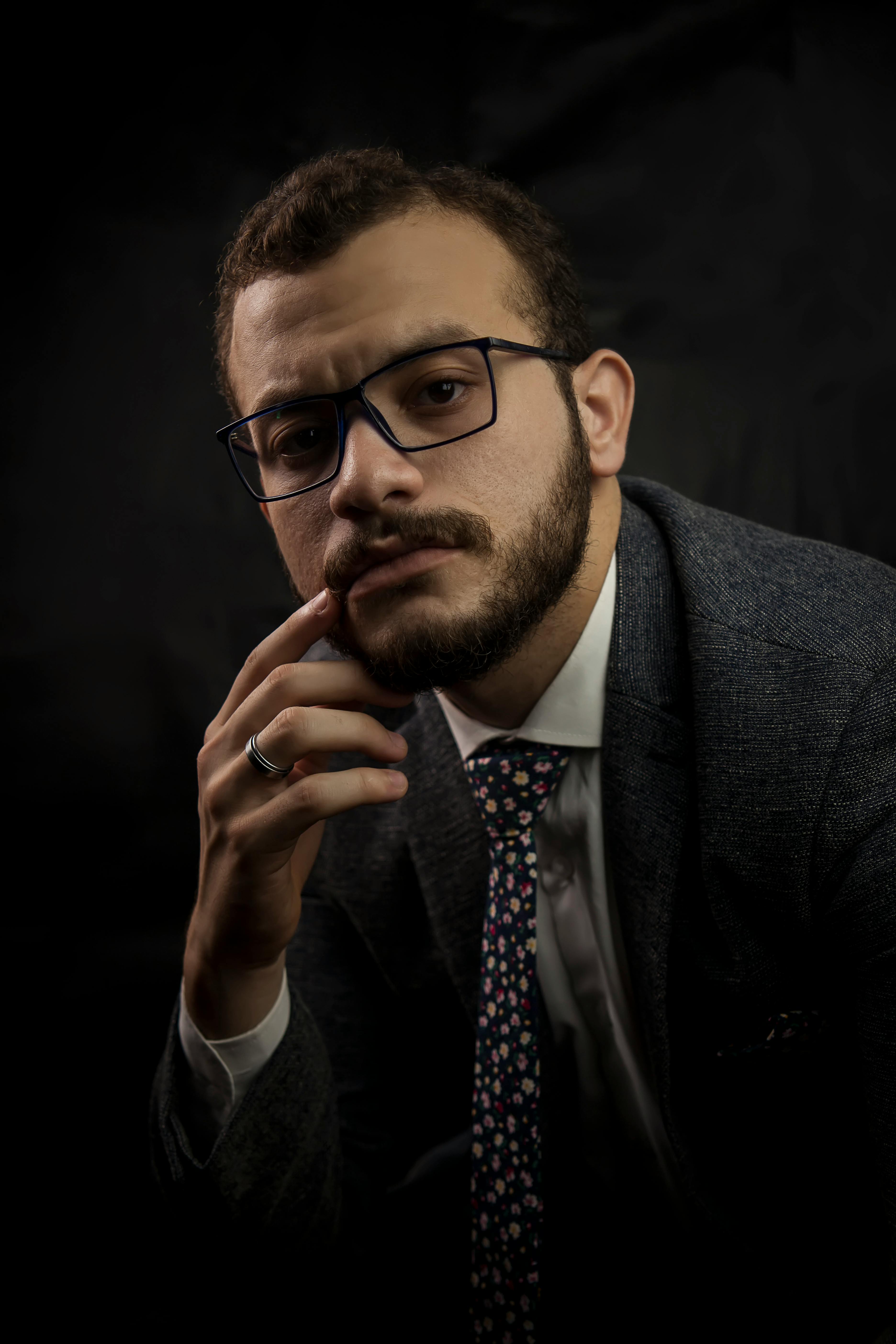 Professional portrait of man in suit and tie with glasses on dark background demonstrating traditional corporate portrait style for NYC professionals