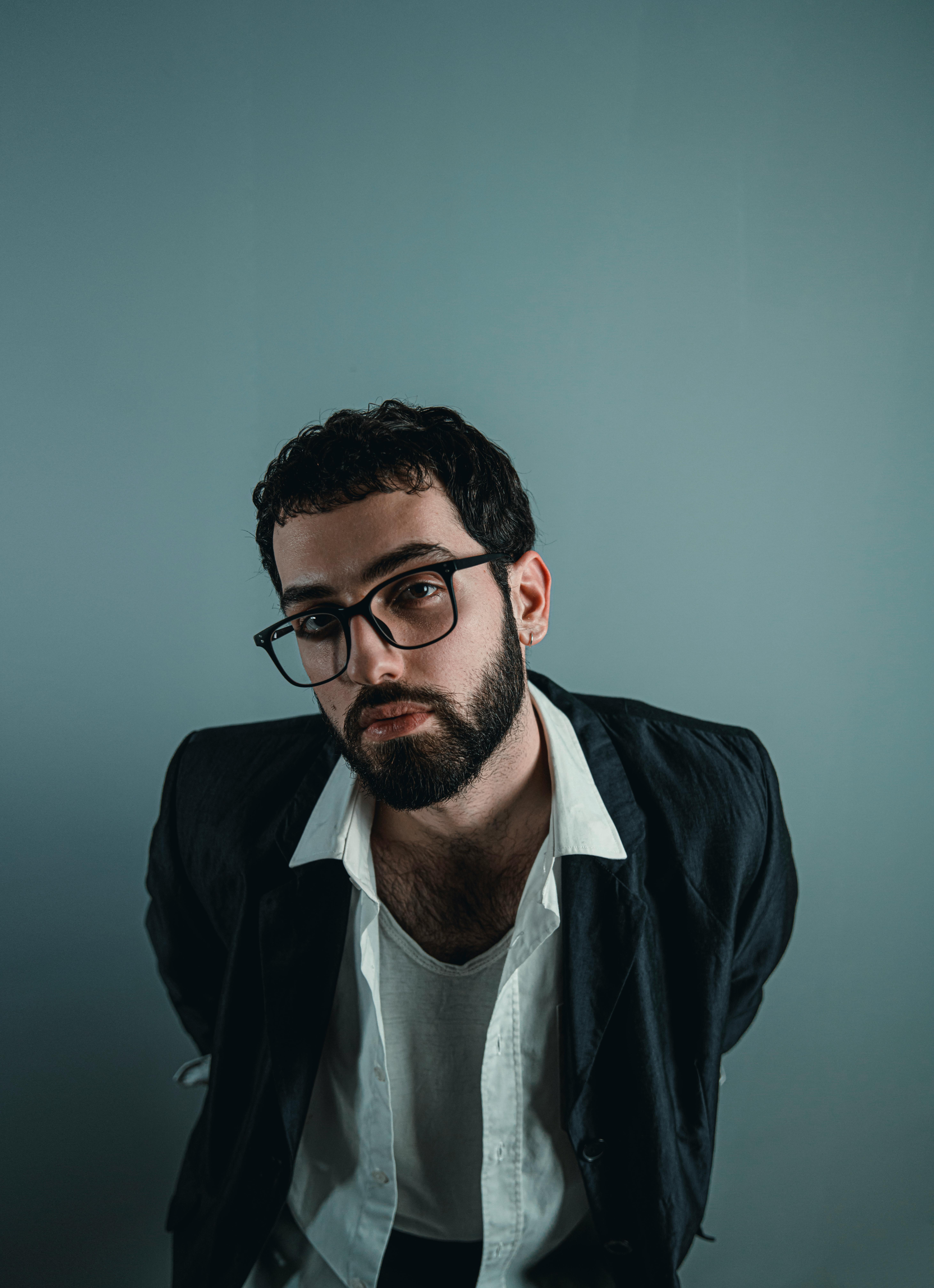 Creative professional portrait of man with glasses and beard in casual jacket and open shirt on minimal background demonstrating modern creative professional style