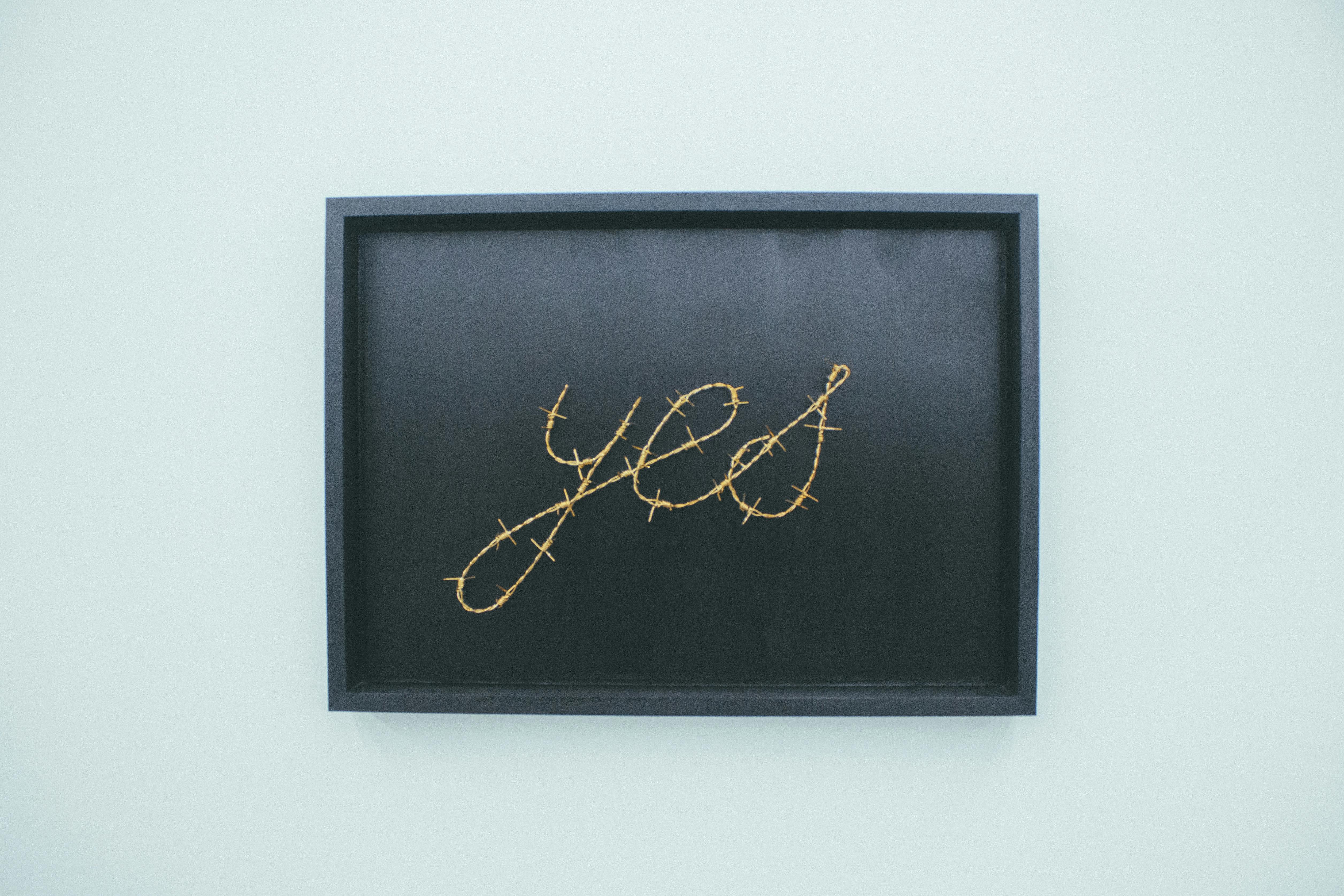 Framed artwork with YES text and barbed wire demonstrating professional gallery framing photography for online sales