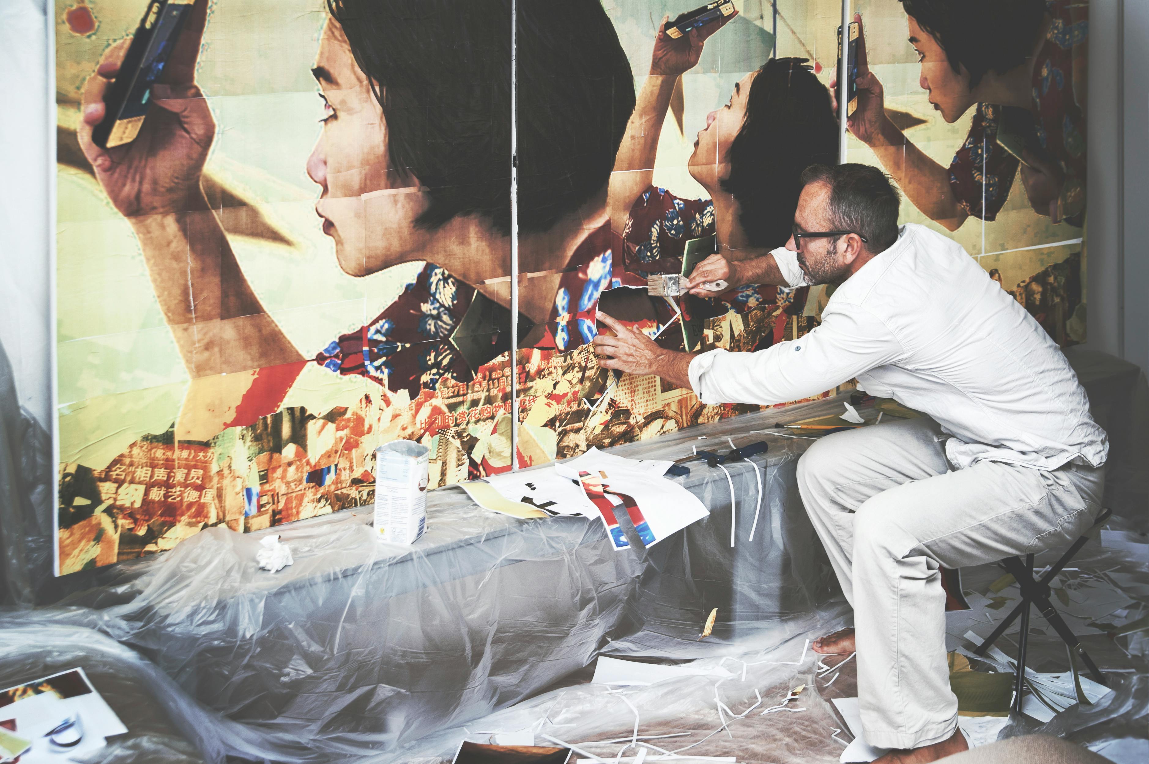 Artist working on large-scale wall mural collage in studio showing scale and process of art creation