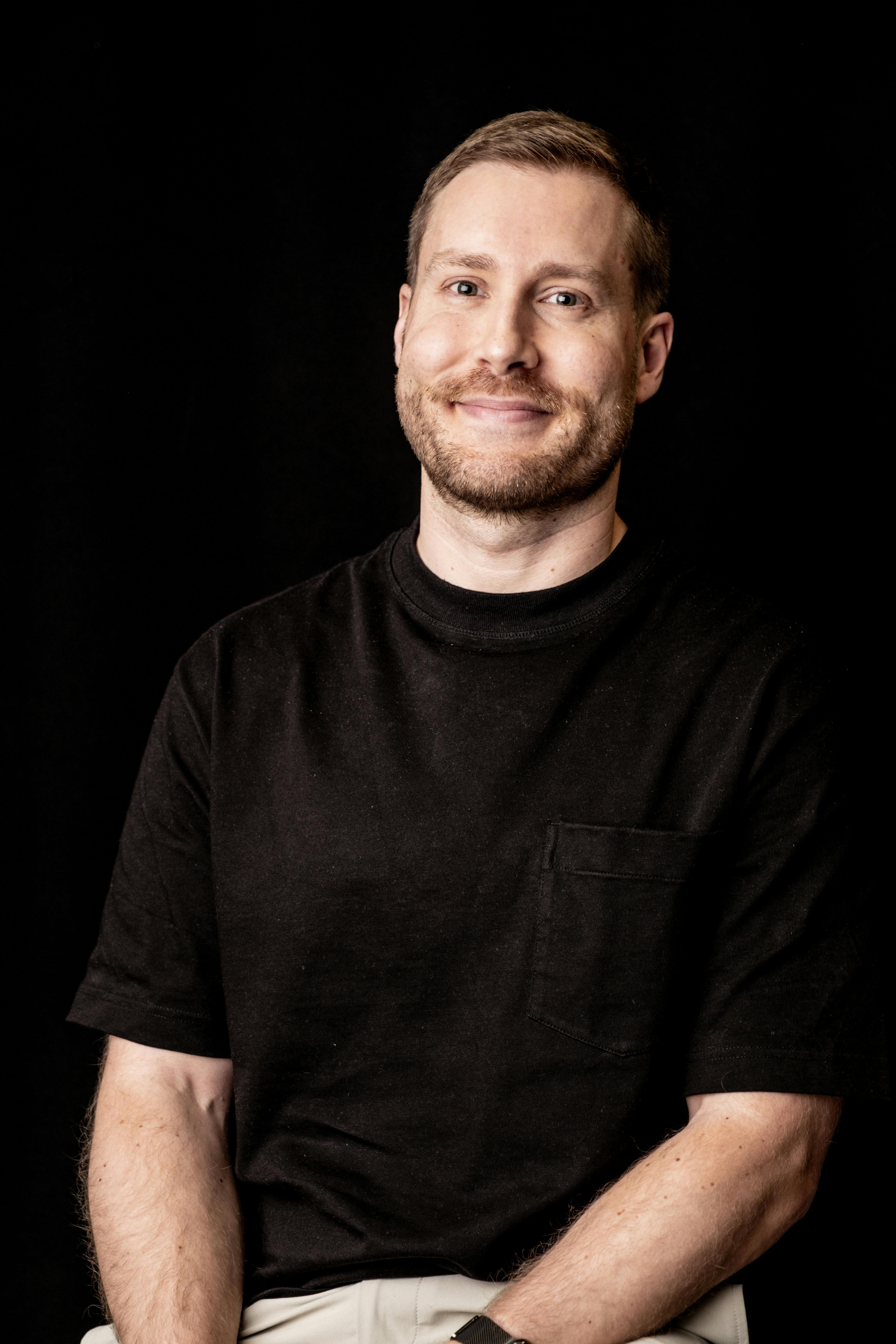 Man in black t-shirt professional headshot with dark background