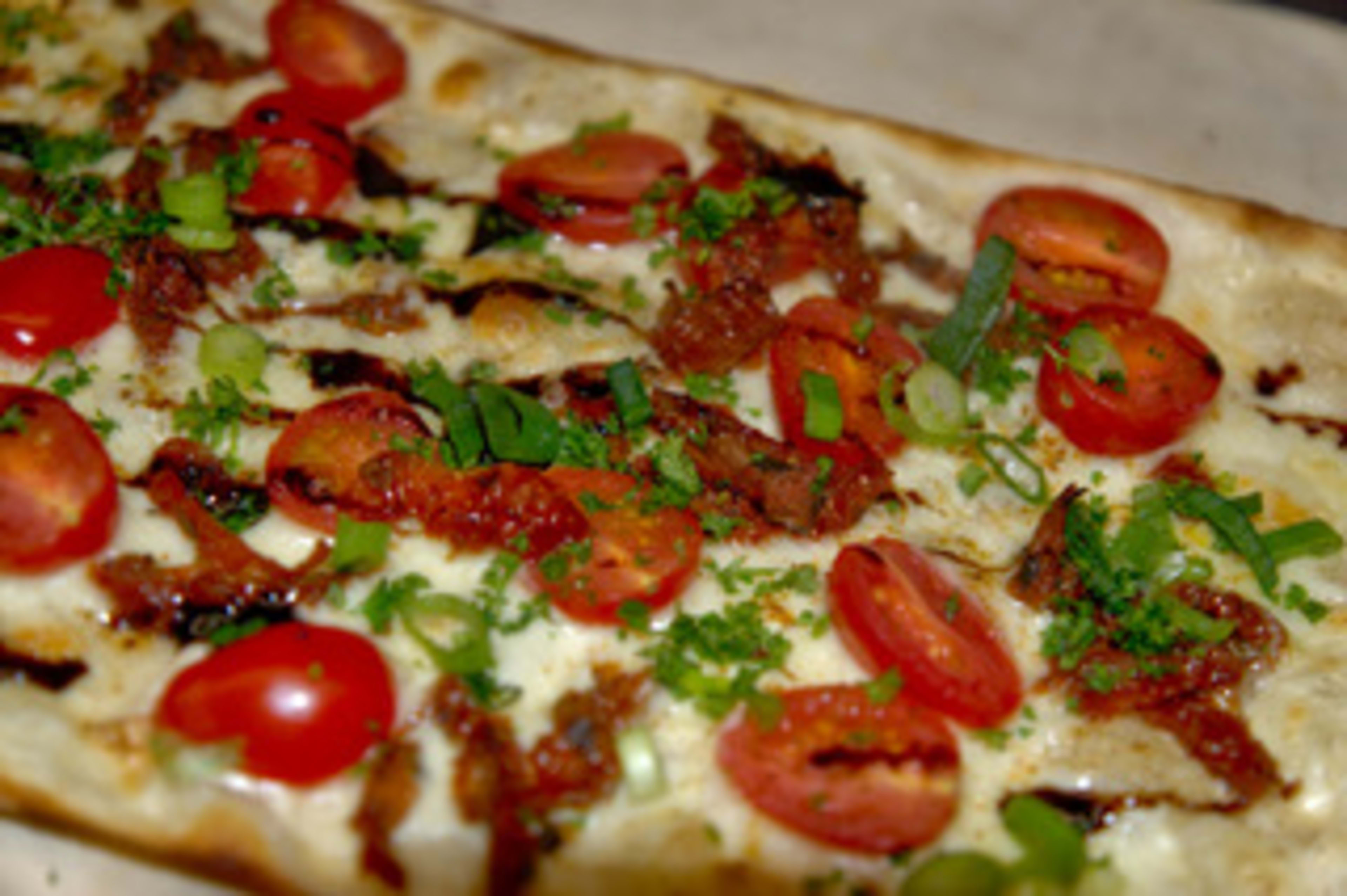 Flammkuchen mit Tomaten, Frühlingszwiebeln, Kräutern und Speckstreifen.