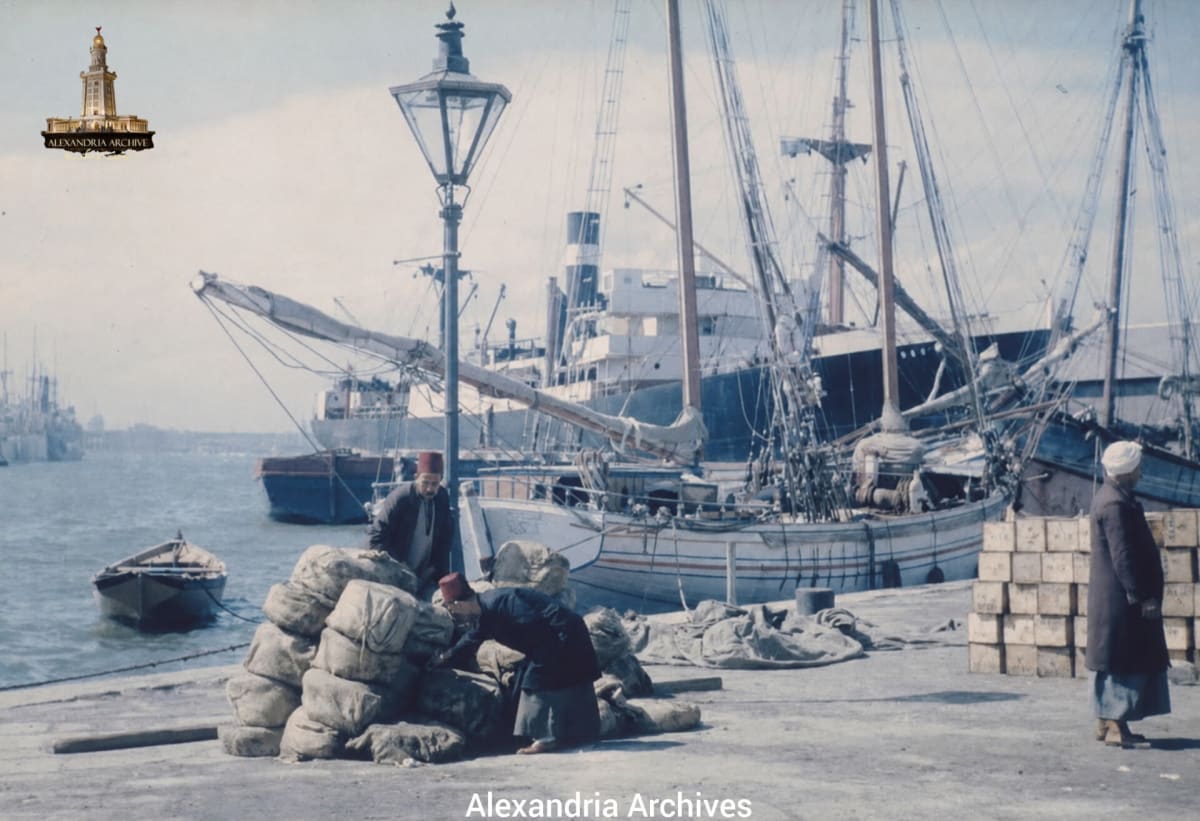 A snapshot from the port of Alexandria, Egypt, circa 1936. The picture shows wooden fishing boats and large cargo ships docked in the port. 