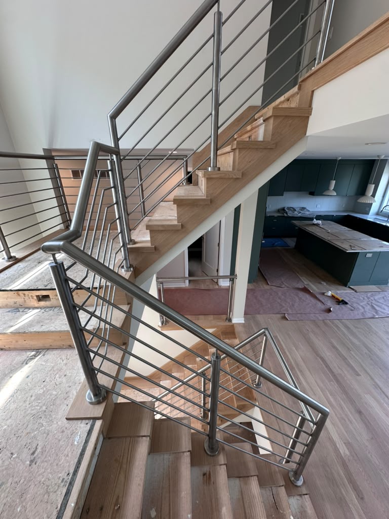 Custom stainless steel staircase railing with horizontal bars installed across multiple flights in a new Warren, MI home
