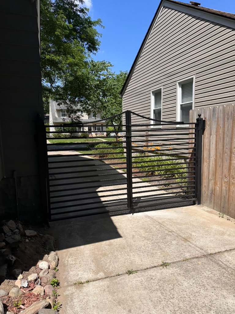 Double swing black metal driveway gate with arched top and horizontal slats, fabricated by Hot Fab Welding in Michigan