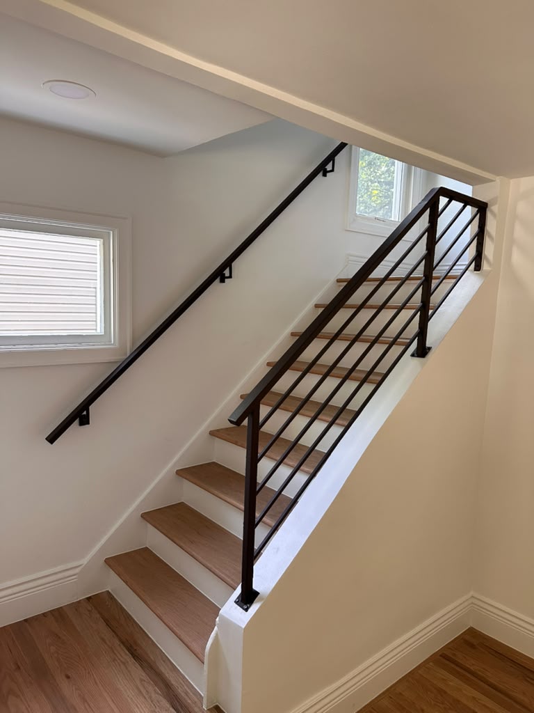 Modern horizontal bar steel staircase railing and handrail on oak stairs, custom fabricated in Michigan